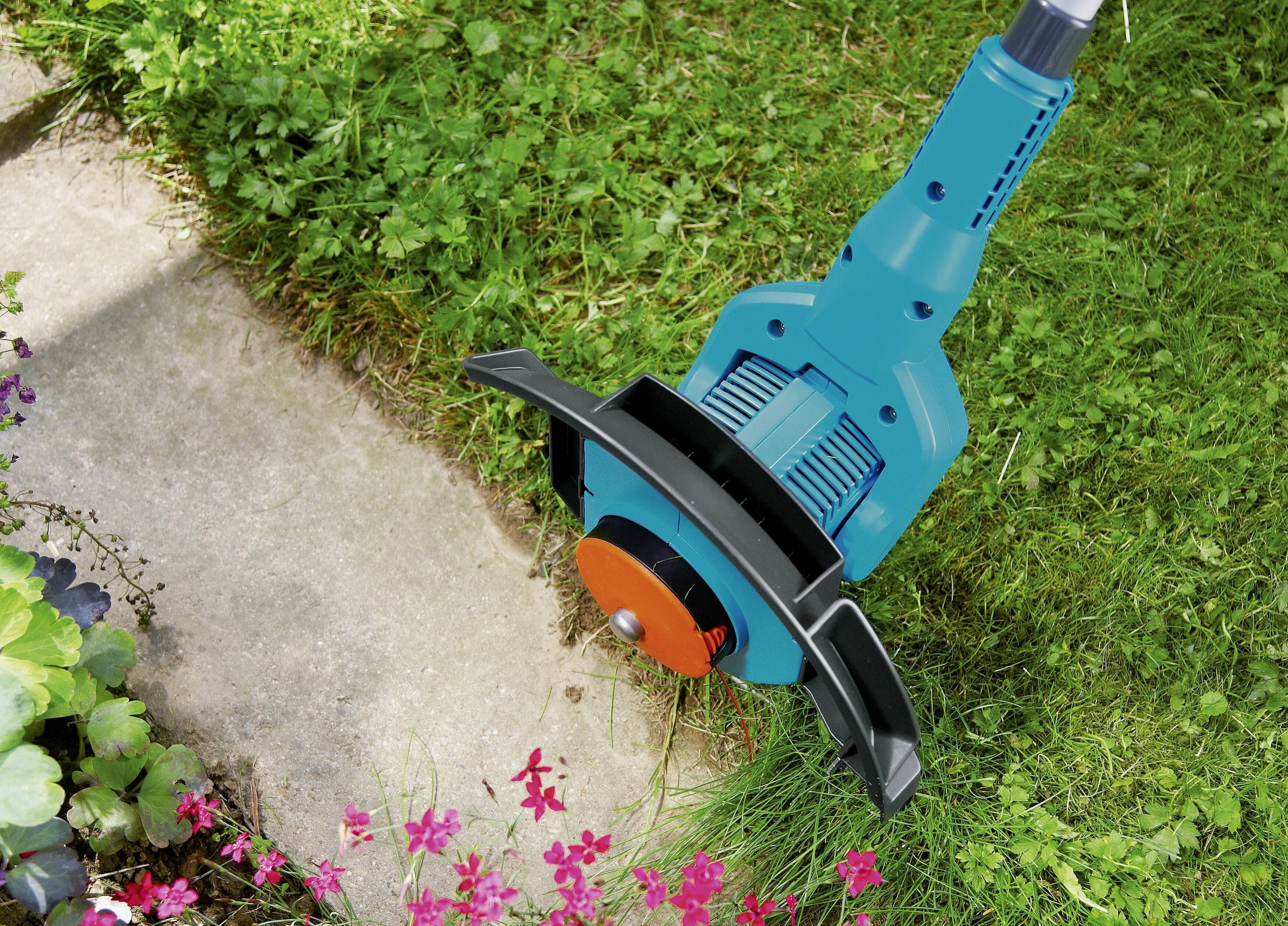 Eine elektrische Gartenschere trimmt präzise die Rasenkante entlang eines gepflasterten Weges in einem Garten.