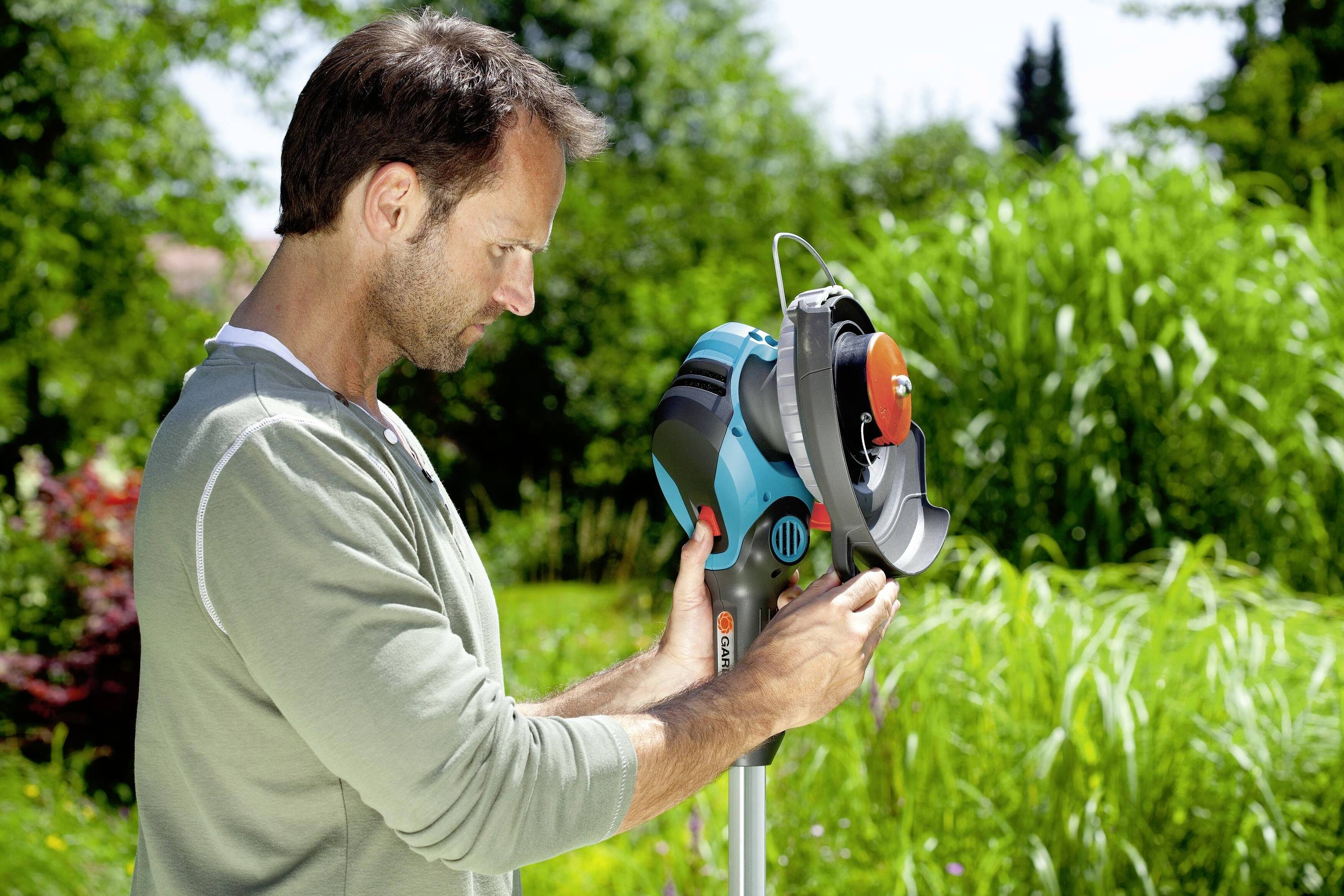 Ein Mann verwendet einen Rasenmäher in einem Garten. Er konzentriert sich auf die Maschine, während er von üppiger Vegetation umgeben ist.