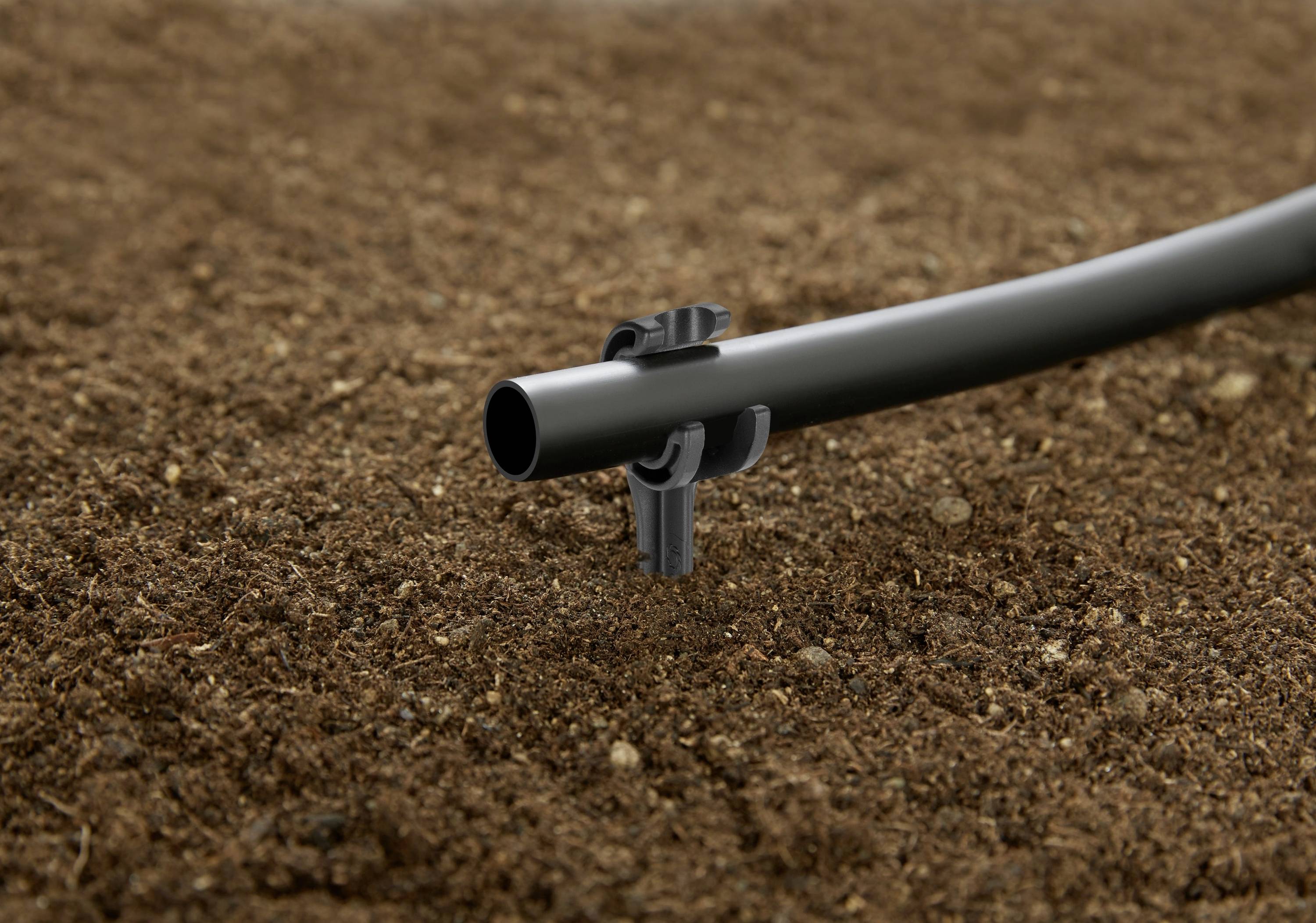 Ein Tropfbewässerungsrohr, das auf dem Boden positioniert und mit einer Klammer befestigt ist und ein effizientes Wasserverteilungssystem für Garten- oder landwirtschaftliche Zwecke veranschaulicht.
