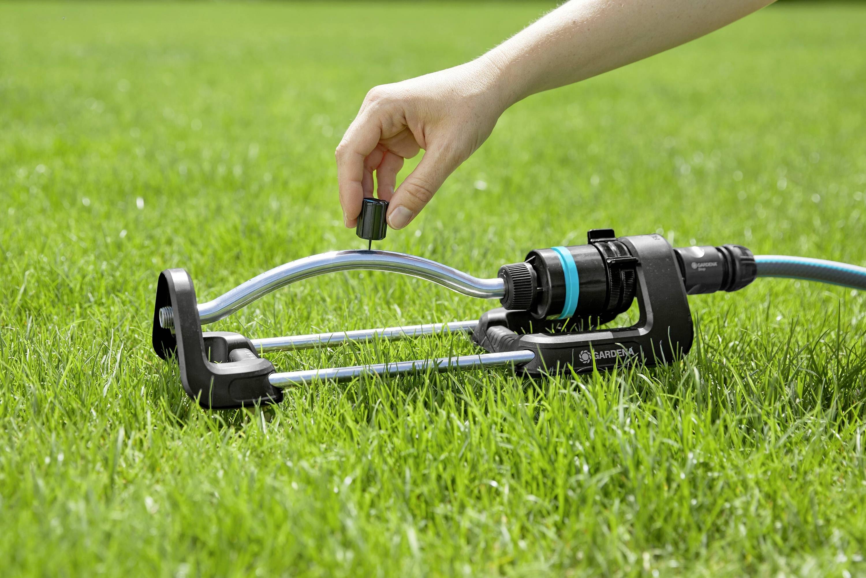 Eine Hand dreht an einem auf dem Rasen liegenden Rasensprenger, um den Wasserstrahl einzustellen.
