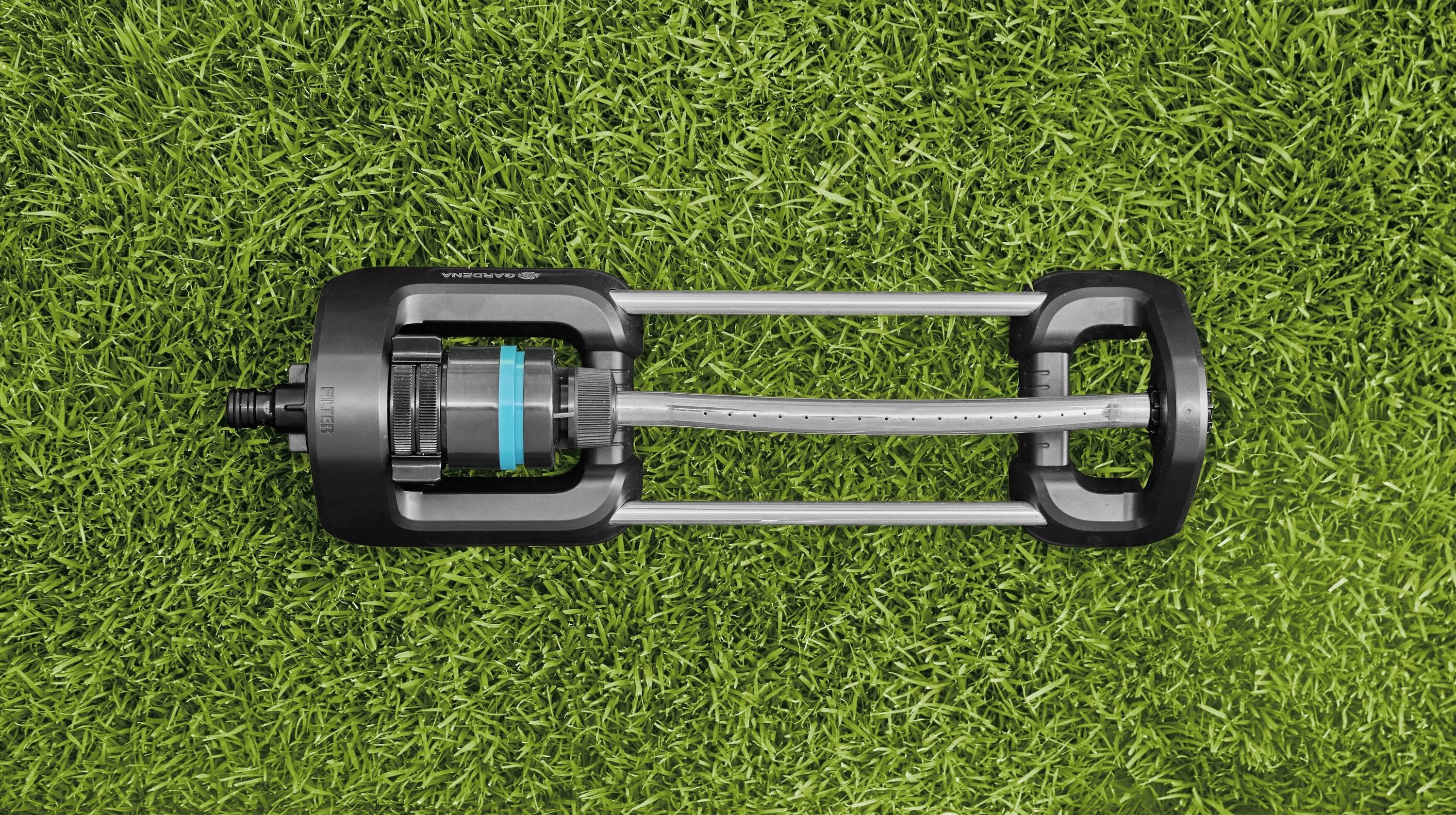 Ein Rasensprenger mit schwarzem und blauem Design liegt auf grünem Gras, bereit zur Bewässerung.