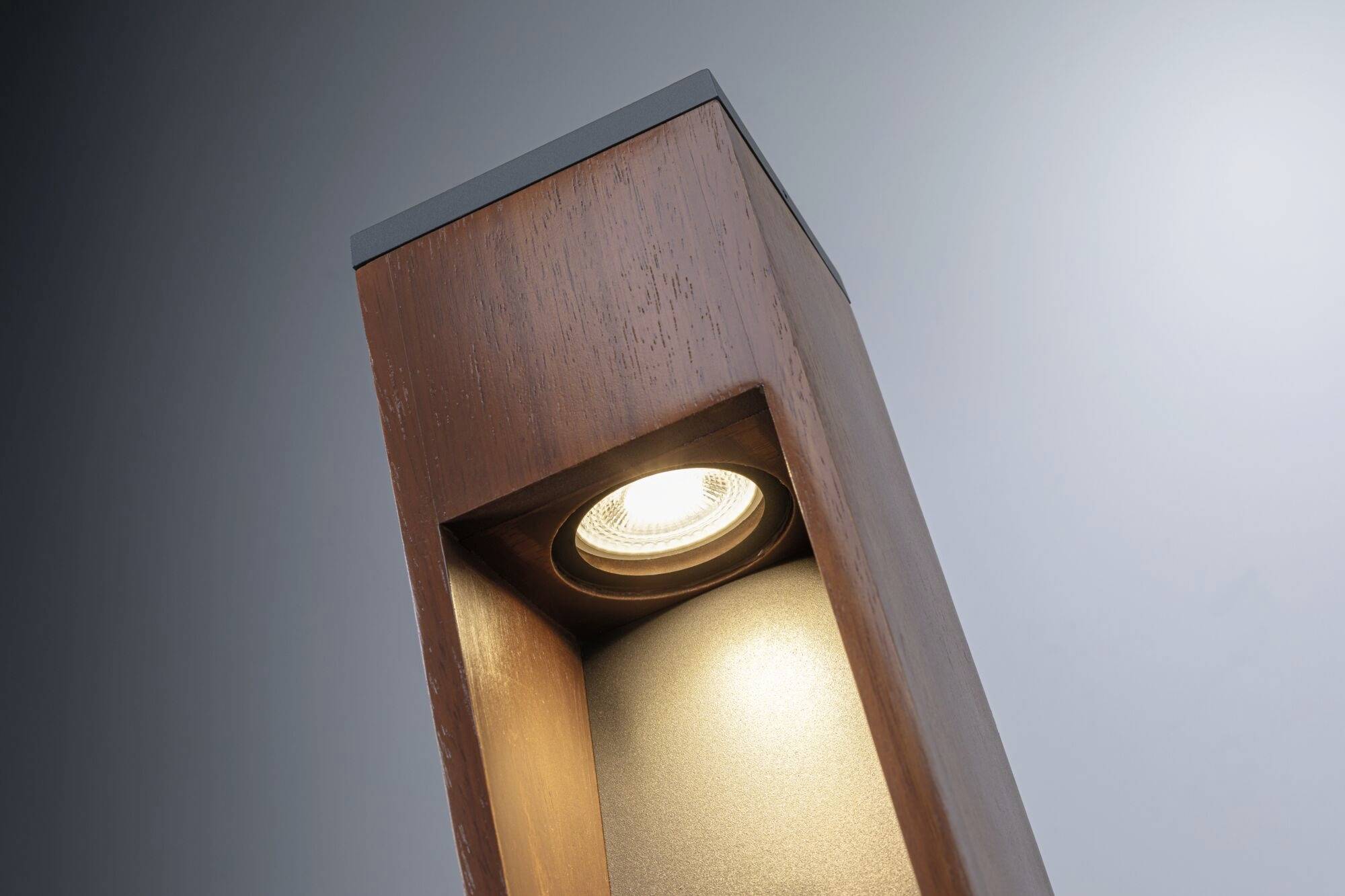 Braune Holzsäule mit eingelassener Lampe oben, leuchtet nach unten. Hintergrund mit blauer Farbverlauf.