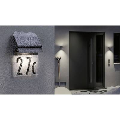 Hausnummer '27c' beleuchtet an einer schneebedeckten Wand. Rechts ein moderner Eingang mit Schneeschaufel daneben.