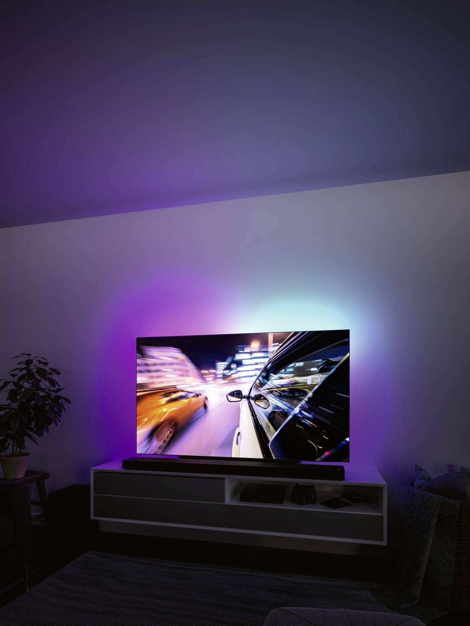 Ein moderner Fernseher zeigt ein Rennen bei Nacht mit leuchtenden Farben, reflektiert das Licht im Raum, und steht auf einem weißen Regal.
