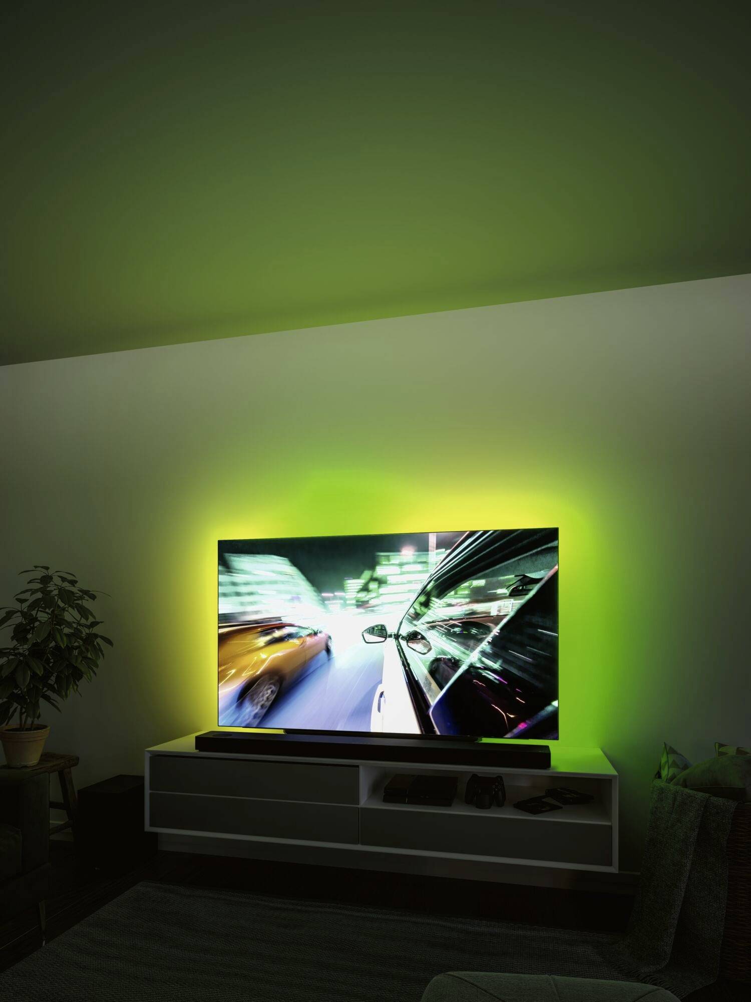 Ein Fernseher zeigt eine rasante Verfolgungsjagd bei Nacht. Das Bild ist von lebendig grünem Licht umgeben, das den Raum beleuchtet.