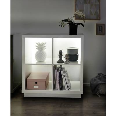 Ein weißes Regal mit vier beleuchteten Fächern enthält eine Ananasfigur, Kerzenhalter, eine Schachtel, Bücher und eine Orchidee.