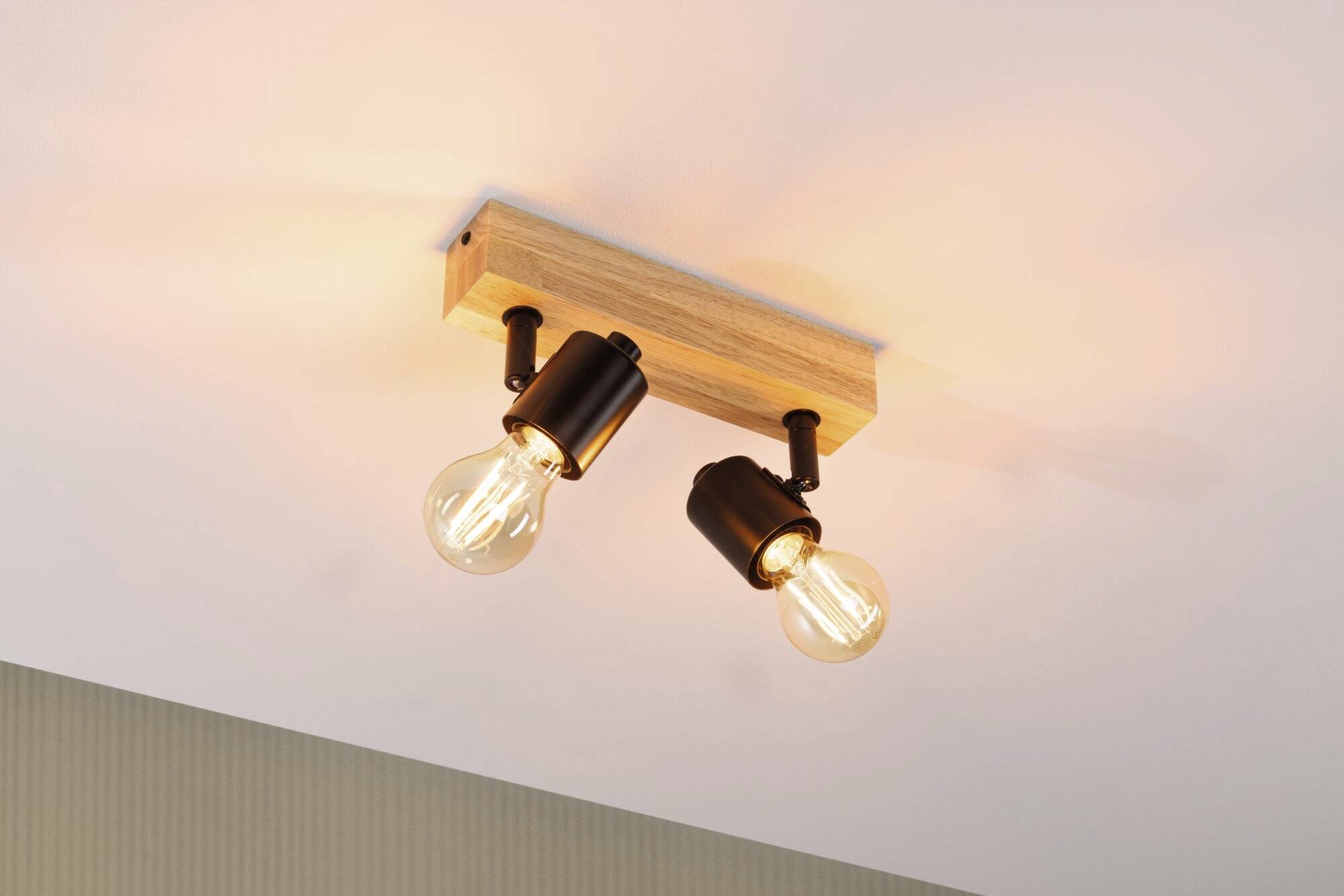 Zwei Glühbirnen in einer modernen, rechteckigen Holzhalterung an der Decke, strahlen warmes Licht aus.