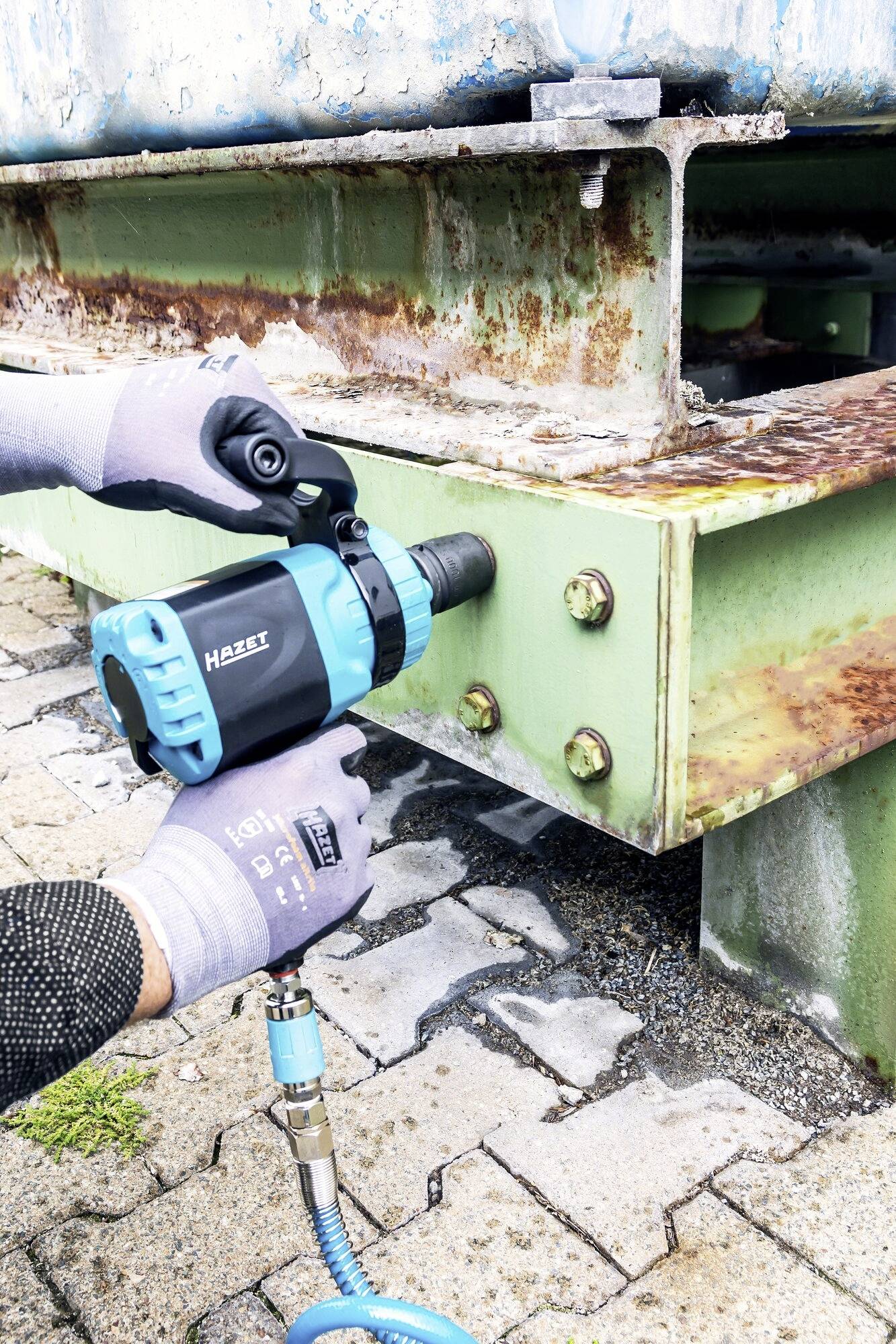 'Man verwendet einen blauen Schlagbohrschrauber, um rostige Schrauben an einem Metallträger im Außenbereich zu befestigen.'