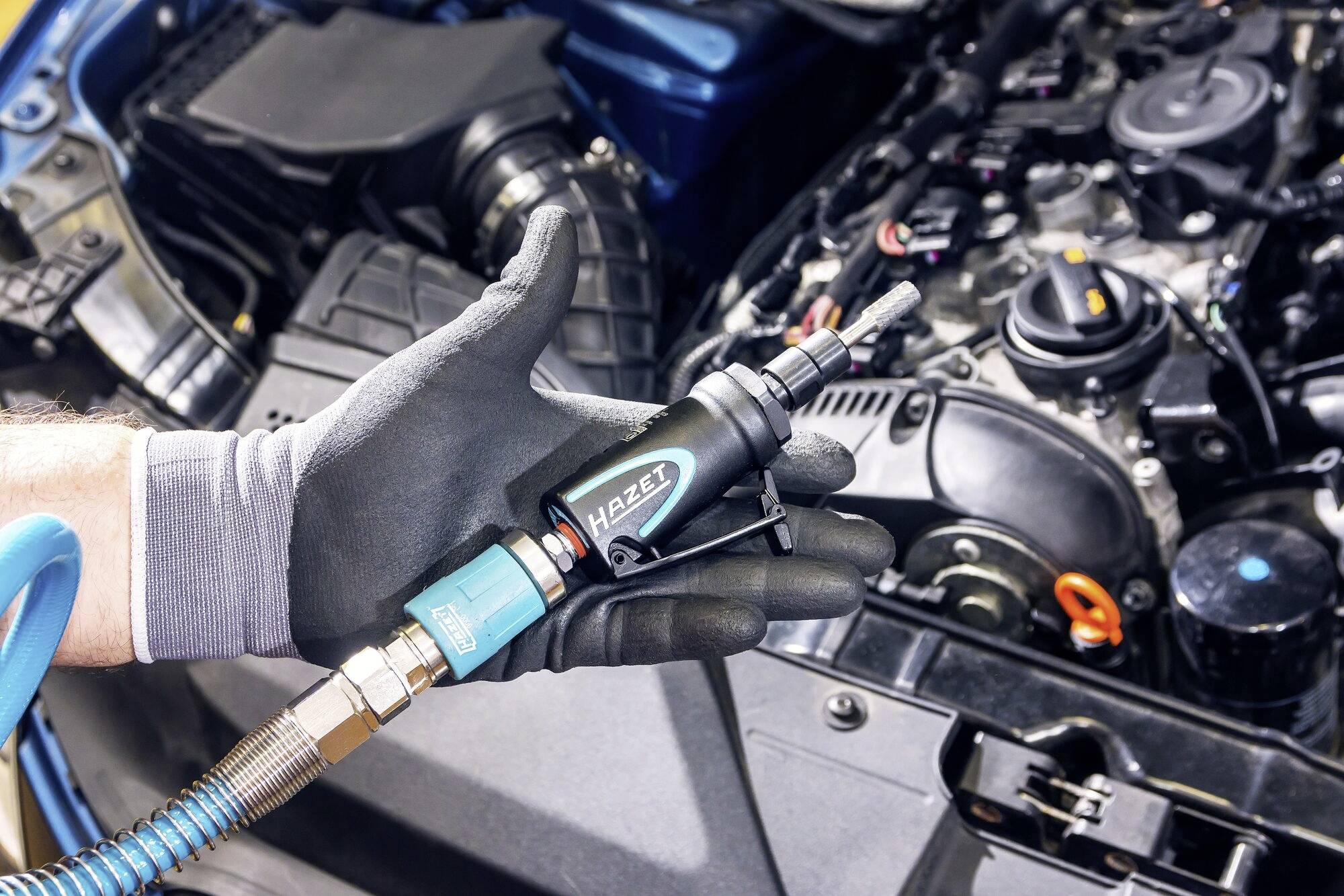 'Hand hält einen Druckluftschrauber vor einem offenen Motorraum eines Autos, bereit zum Einsatz bei Wartungsarbeiten.'