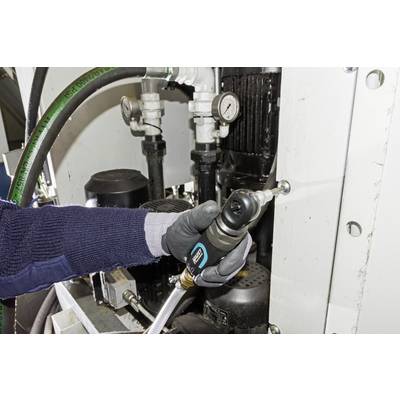 Eine Person mit Handschuhen benutzt ein Werkzeug, um eine Maschine zu warten. Verschiedene Rohre und Manometer sind zu sehen.