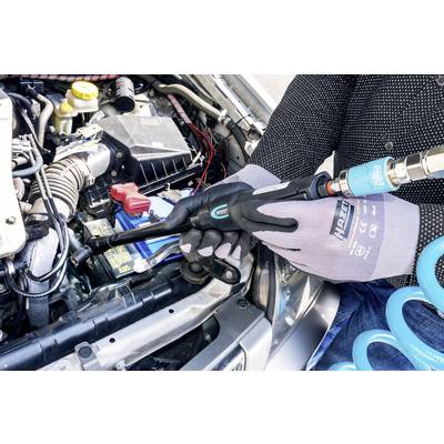 Eine Person prüft den Motor eines Autos mit einem Messgerät, während sie Schutzhandschuhe trägt. Der Motorraum ist detailliert sichtbar.