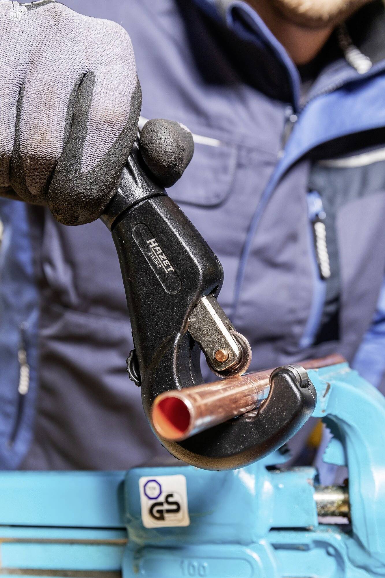 Ein Handwerker schneidet ein Kupferrohr mit einem Rohrschneider. Das Rohr ist in einem Schraubstock eingespannt.