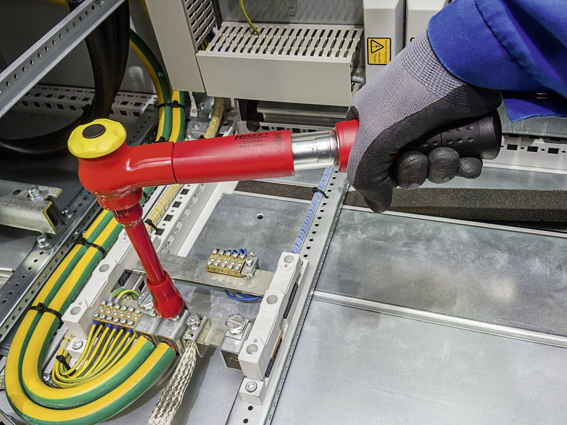 Eine Person mit Handschuh nutzt einen Drehmomentschlüssel, um an einer elektrischen Anschlussklemme in einem Schaltschrank zu arbeiten.