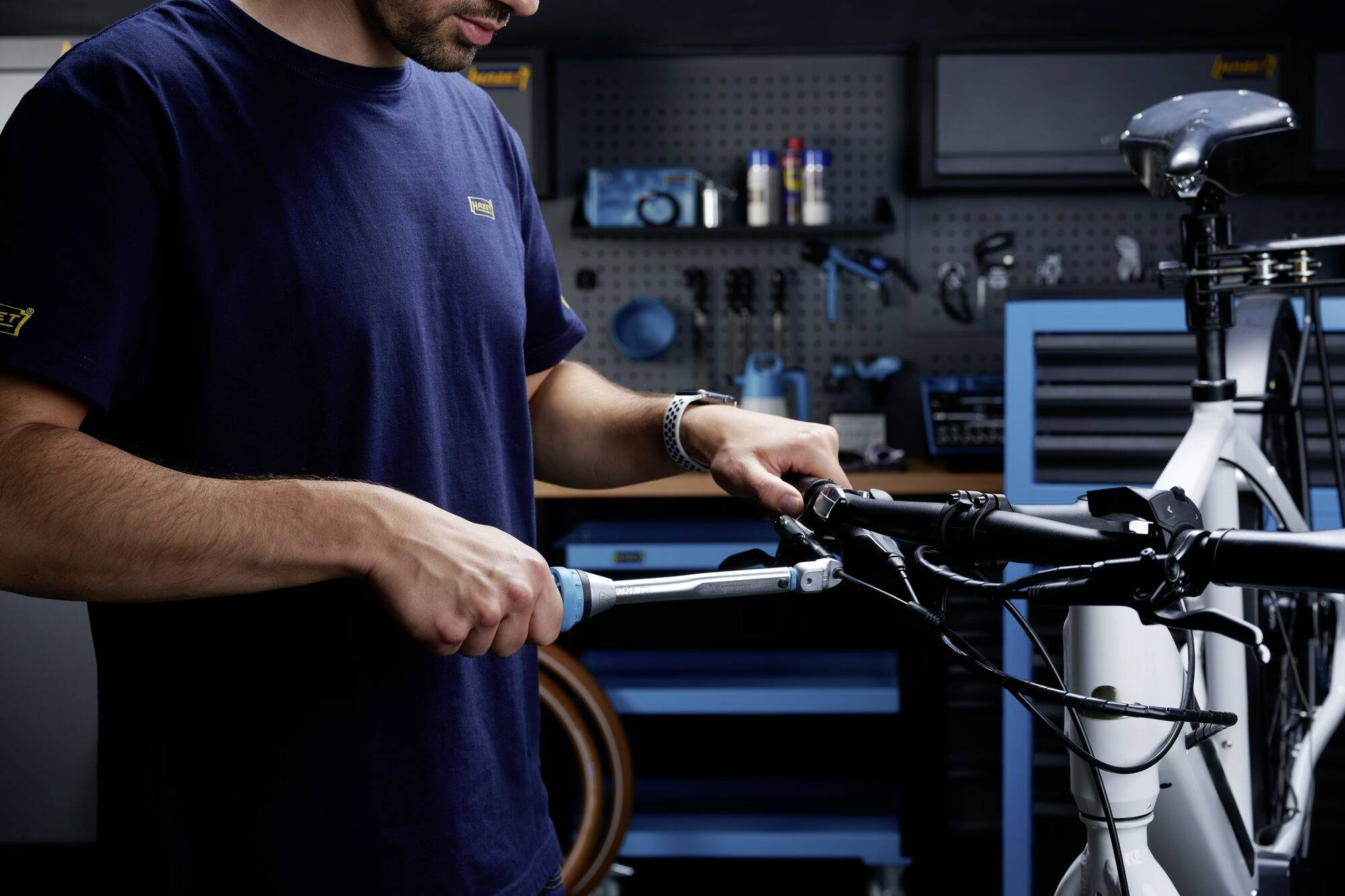 Ein Mechaniker repariert ein Fahrrad in einer Werkstatt. Er verwendet ein Werkzeug, um das Lenkrad einzustellen. Werkzeuge hängen im Hintergrund an der Wand.