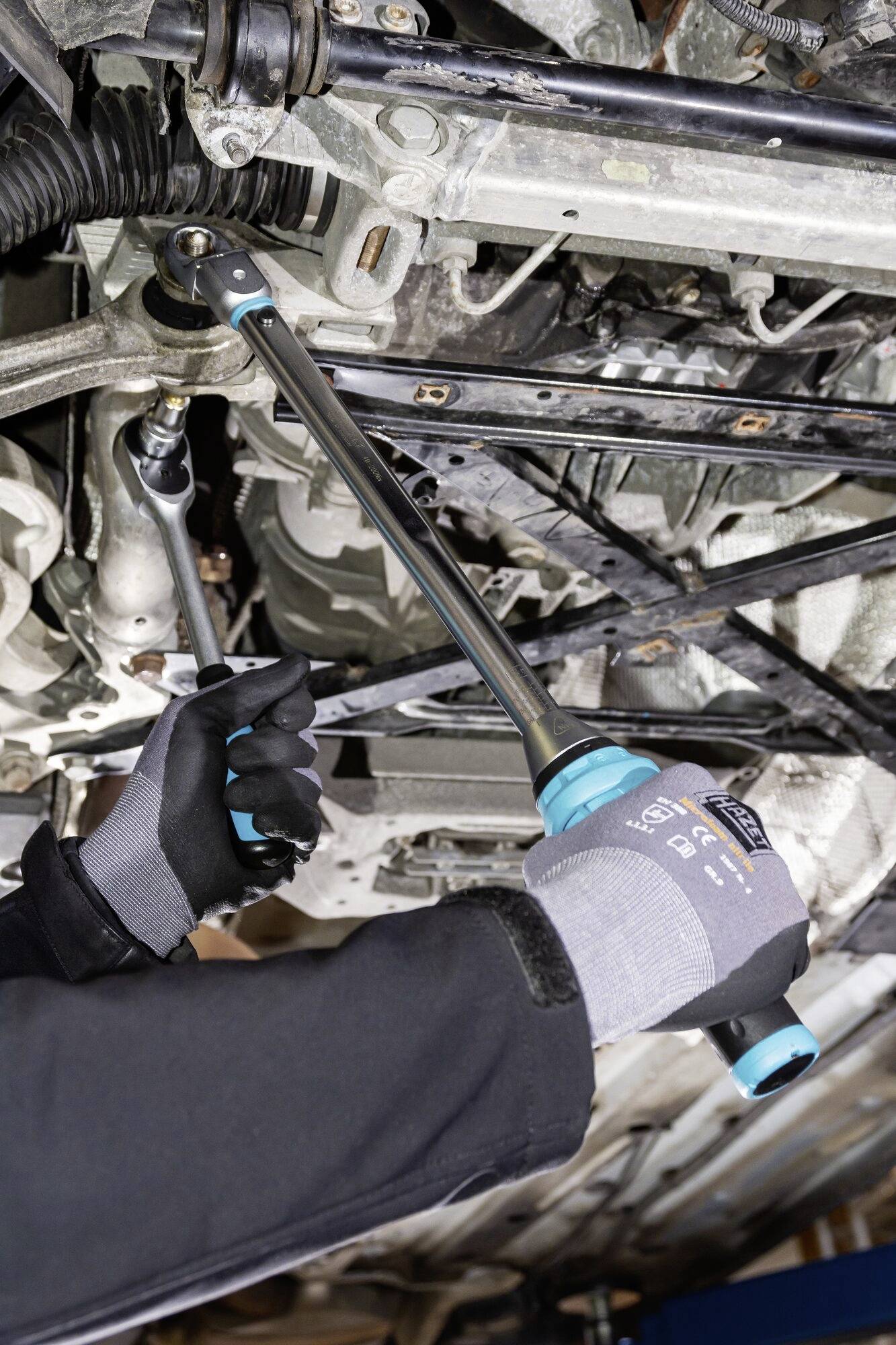 Mechaniker repariert das Fahrwerk eines Autos mit einem Drehmomentschlüssel. Hände in Sicherheitshandschuhen greifen das Werkzeug.