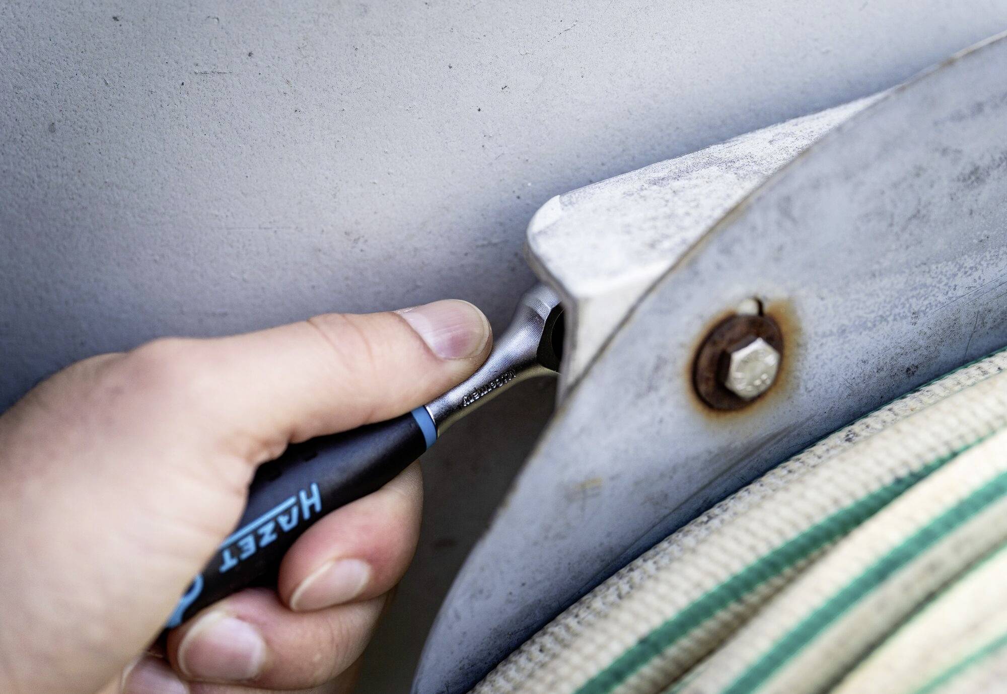 Eine Hand zieht mit einem blauen Schraubenschlüssel eine Schraube an einer Metallhalterung fest.
