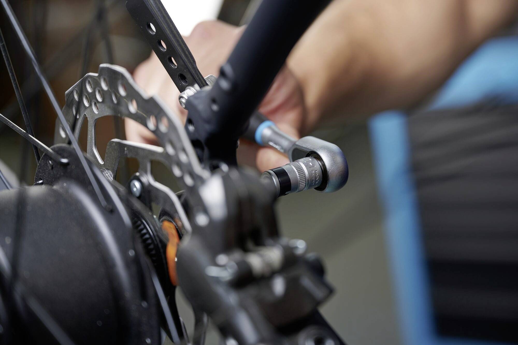 Eine Person zieht mit einem Schraubenschlüssel eine Schraube an einem Fahrrad-Laufrad an, nahe der Bremsscheibe.