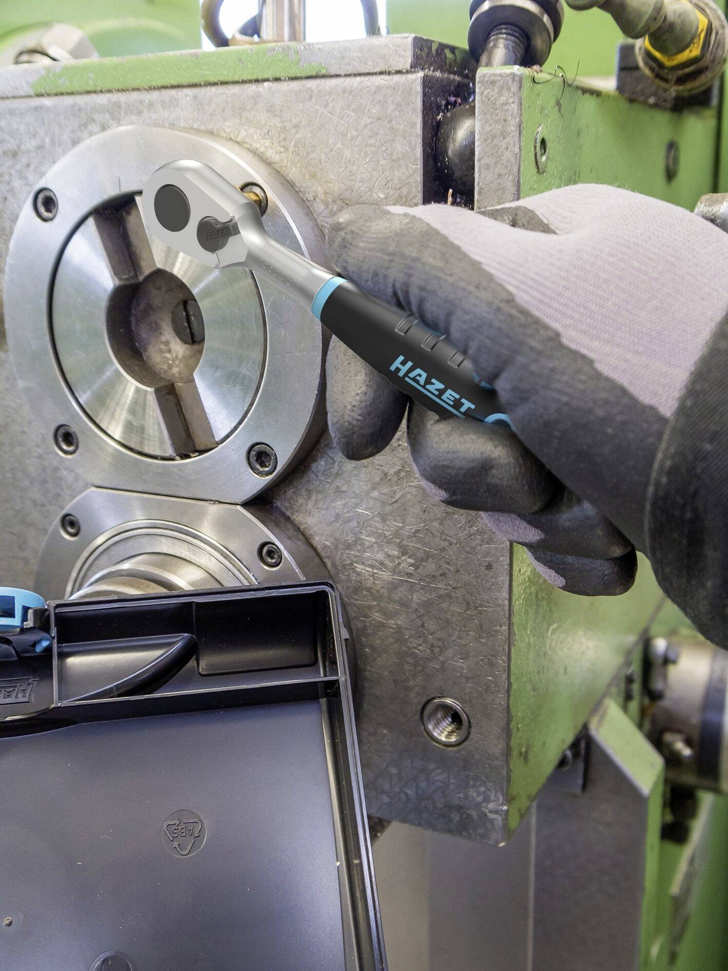 Ein Mechanikerhand mit Handschuh dreht mit einem Drehmomentschlüssel eine Schraube an einer Metallmaschine fest.