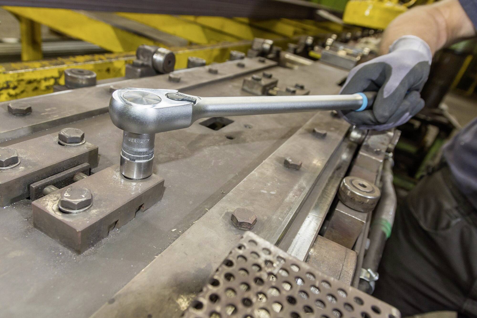 Eine Person benutzt einen Schraubenschlüssel, um eine große Metallmaschine in einer industriellen Umgebung anzuziehen.