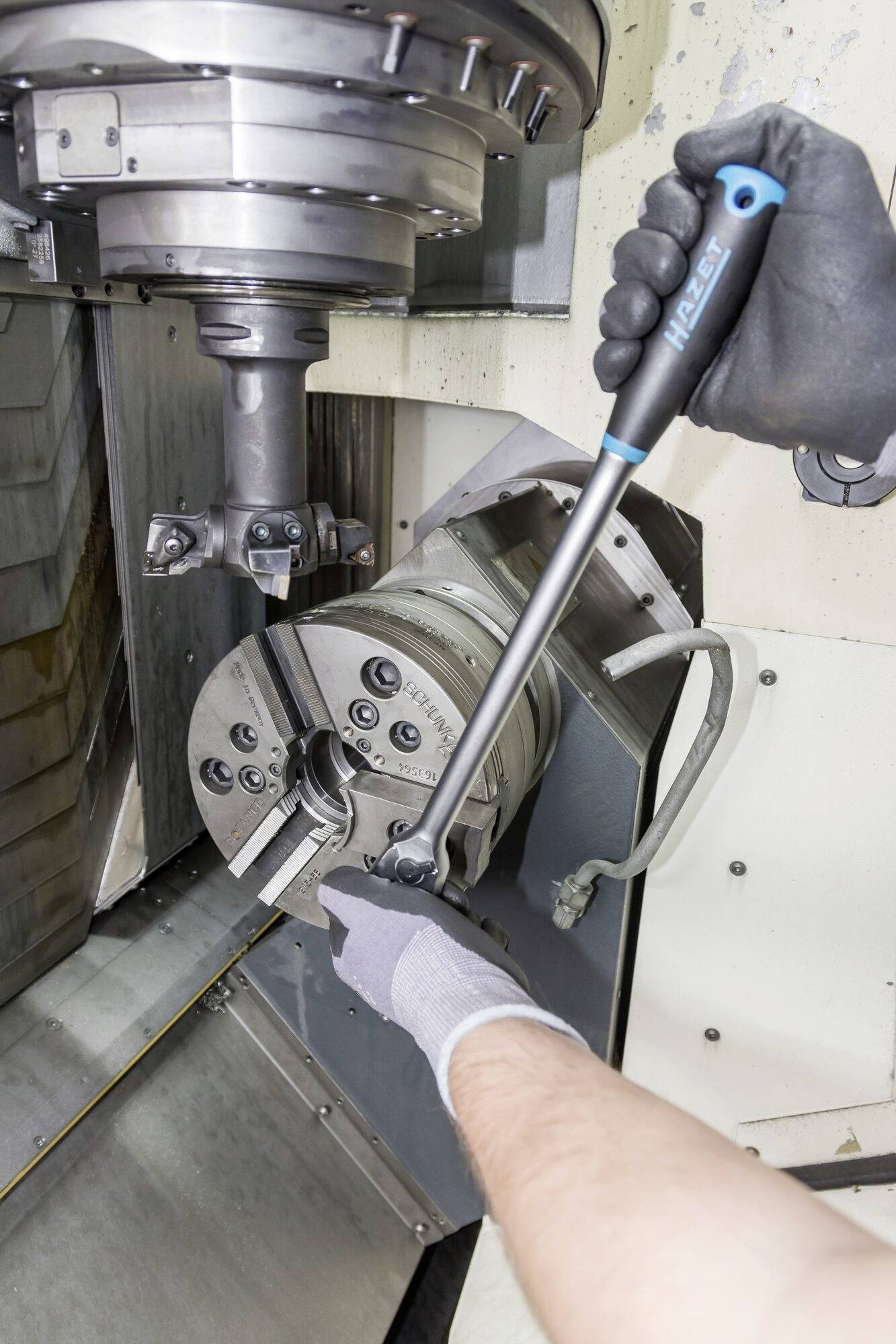 Eine Person befestigt mit einem Drehmomentschlüssel ein Werkstück in einer CNC-Maschine, möglicherweise in einer industriellen Umgebung.