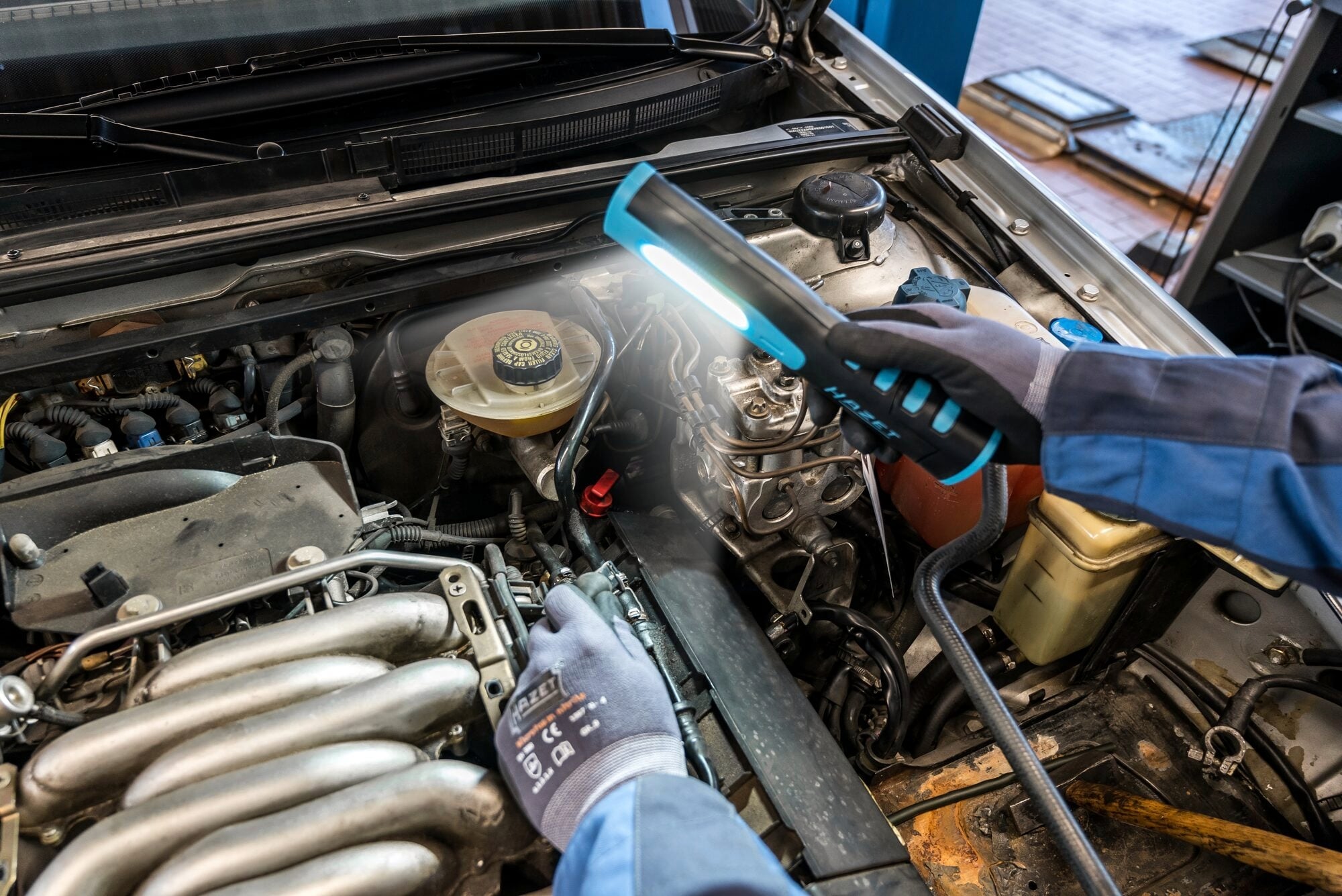 Mechaniker inspiziert den Motorraum eines Autos mit einer Taschenlampe, um Wartungsarbeiten durchzuführen.