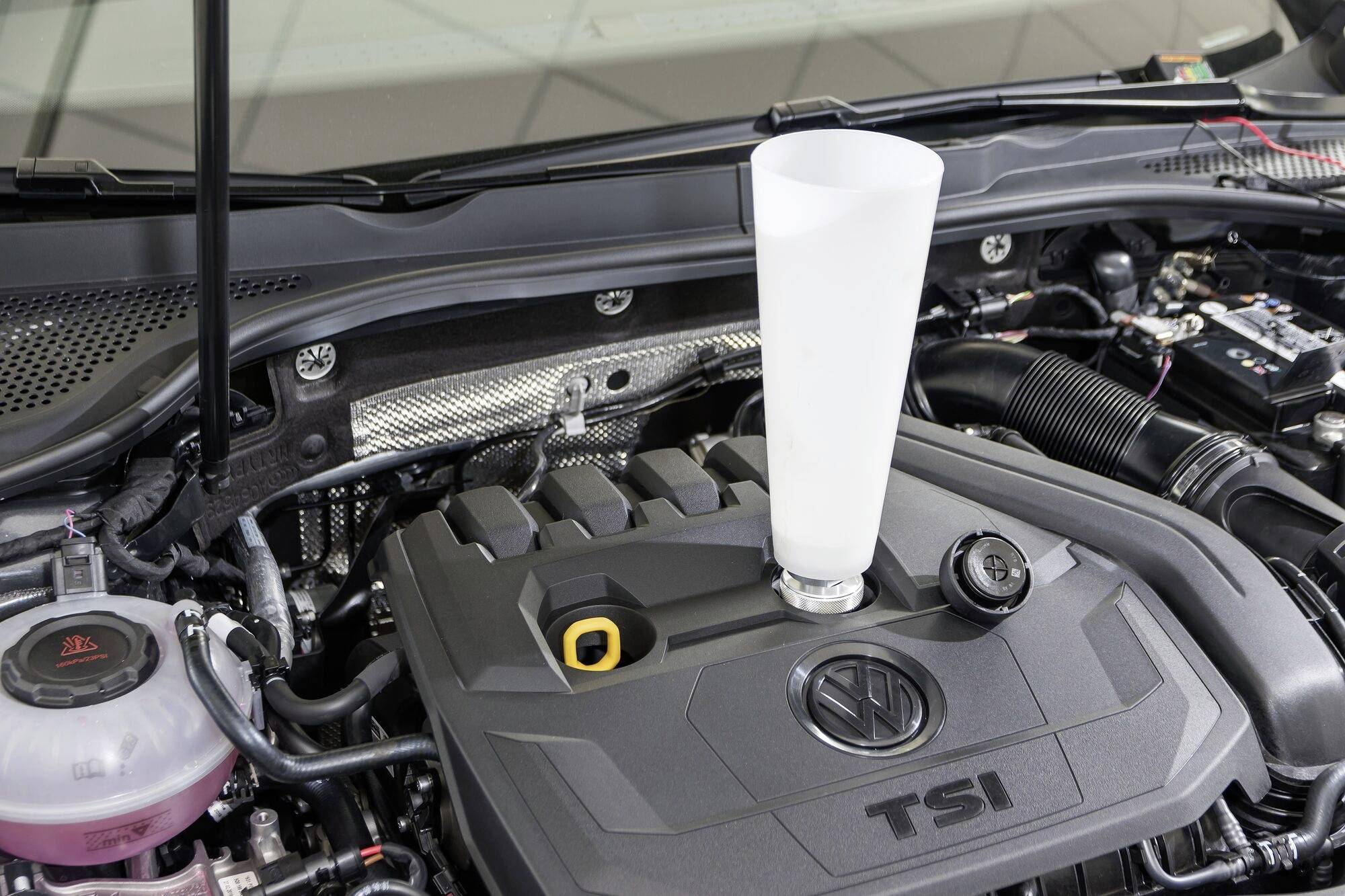 Motorhaube eines Autos geöffnet, ein weißer Trichter steckt im Öl-Einfüllstutzen des Motors, der mit 'TSI' markiert ist.