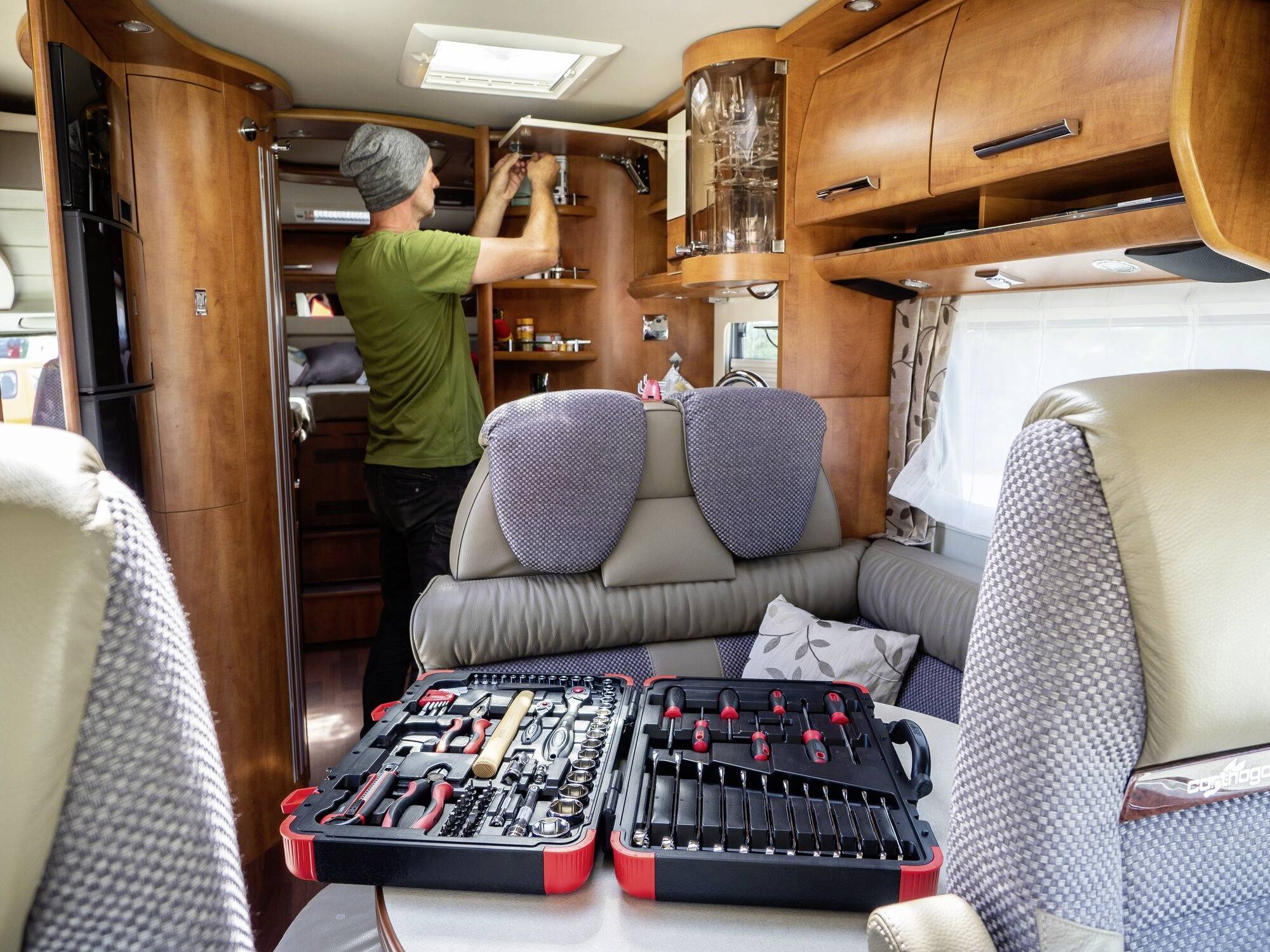 Ein Mann arbeitet in einem Wohnmobil an einem Regal. Auf einem Tisch liegt ein geöffneter Werkzeugkasten.