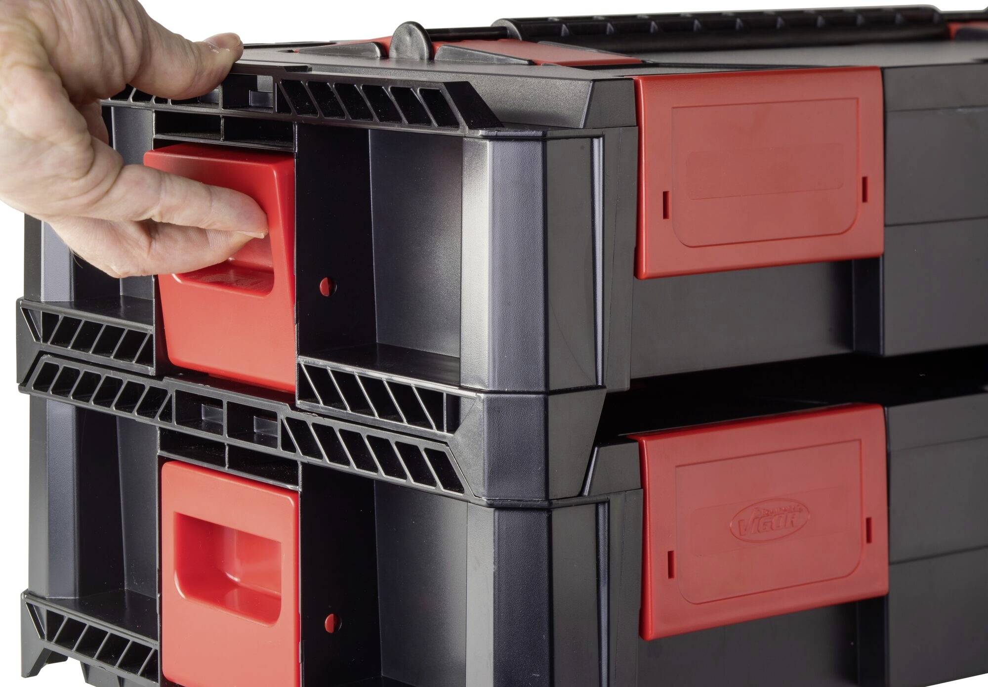Eine Hand zieht an einem roten Griff einer schwarzen Werkzeugbox. Die Box hat zwei übereinander gestapelte Einheiten mit roten Verschlüssen.