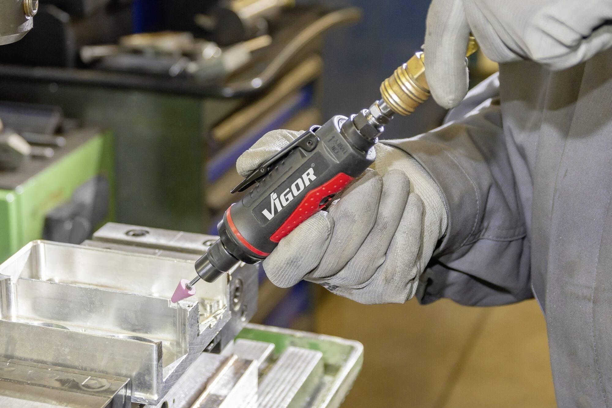 Eine Person bearbeitet ein Metallteil mit einem Druckluftschleifer in einer Werkstatt.