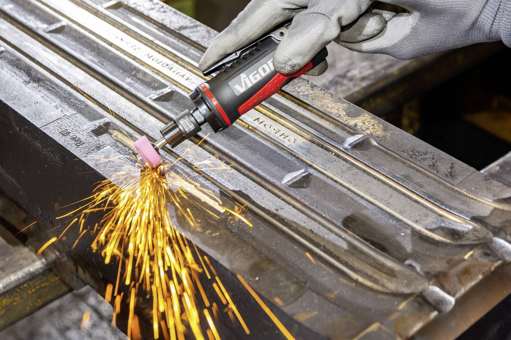 Eine Person schleift Metall mit einem Elektrowerkzeug, während Funken sprühen. Die Szene zeigt eine präzise Industrietätigkeit.