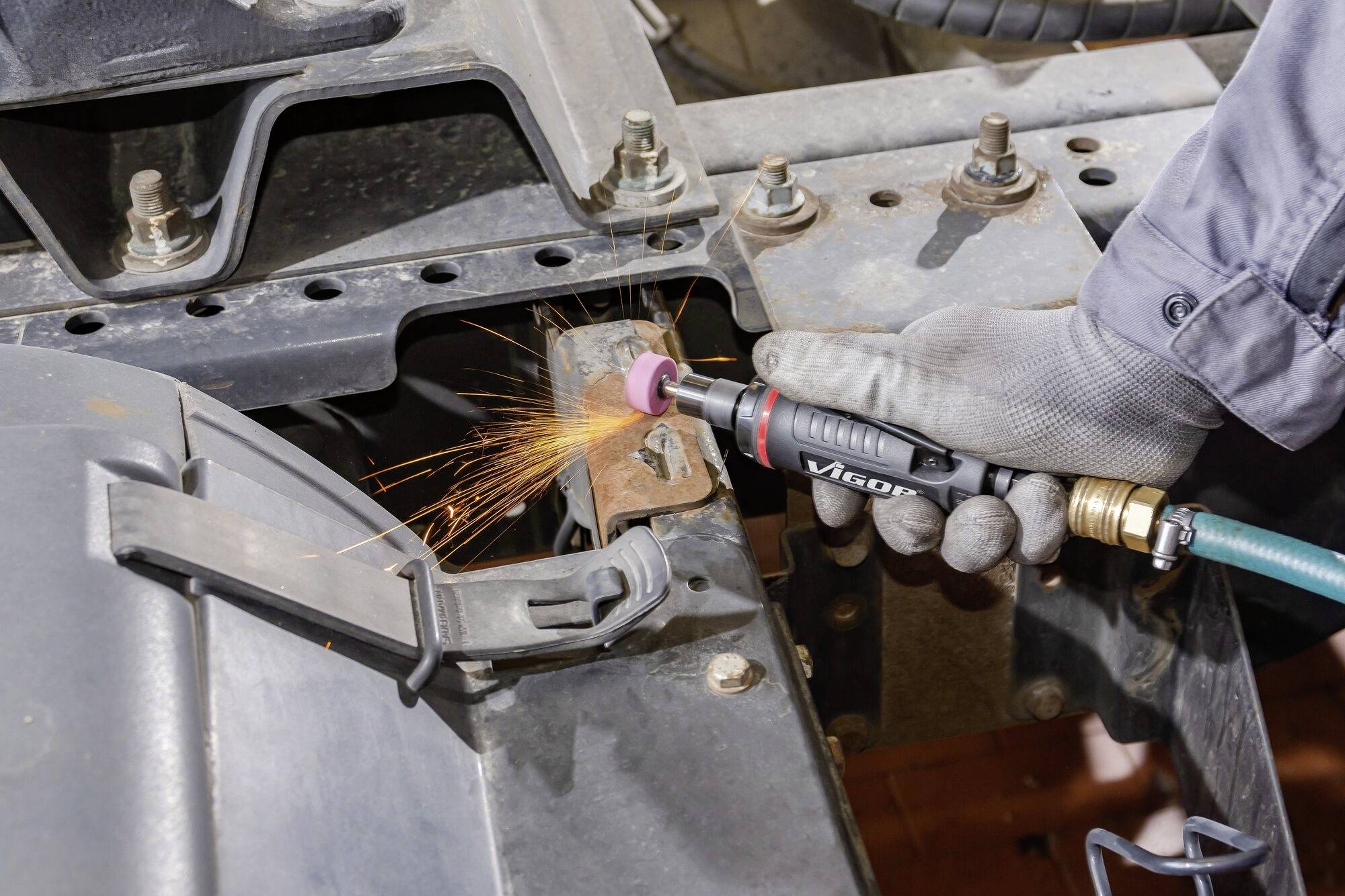 Eine Person verwendet ein Werkzeug, um Metall zu schleifen, während Funken sprühen. Der Arbeitsplatz ist auf einem metallischen Rahmen.