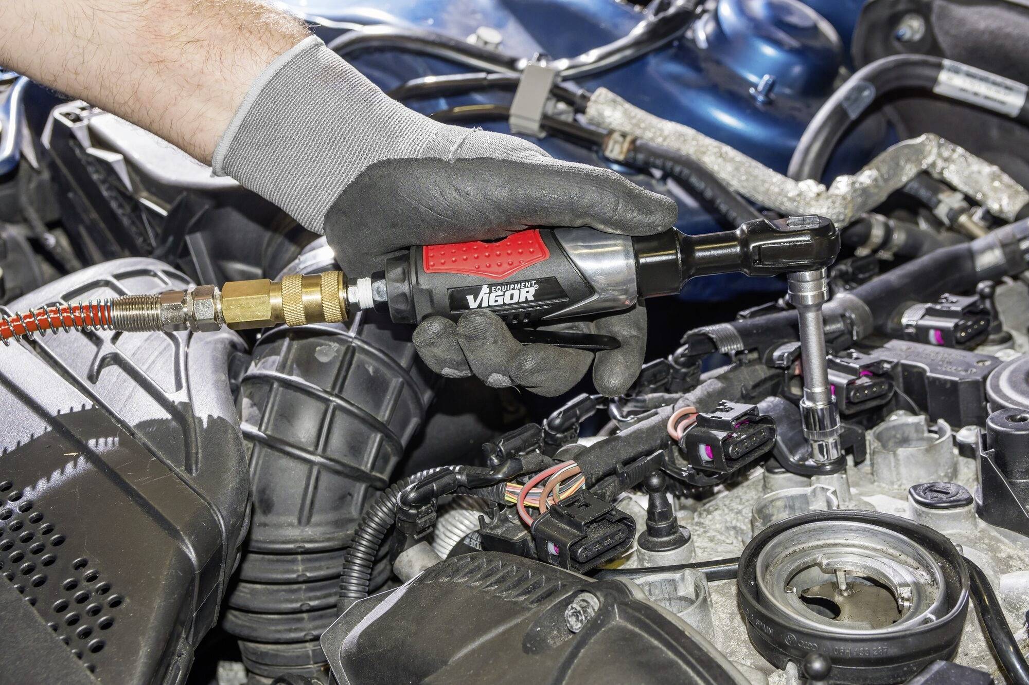 Eine Person repariert einen Motor mit einem Druckluft-Schlagschrauber. Der Fokus liegt auf der Wartung eines Fahrzeugteils.