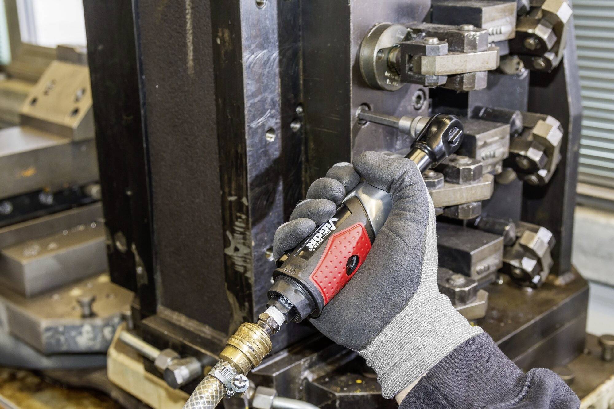 Eine Person in Arbeitshandschuhen hält ein elektrisches Werkzeug an eine Metallmaschine, möglicherweise zur Reparatur oder Montage.