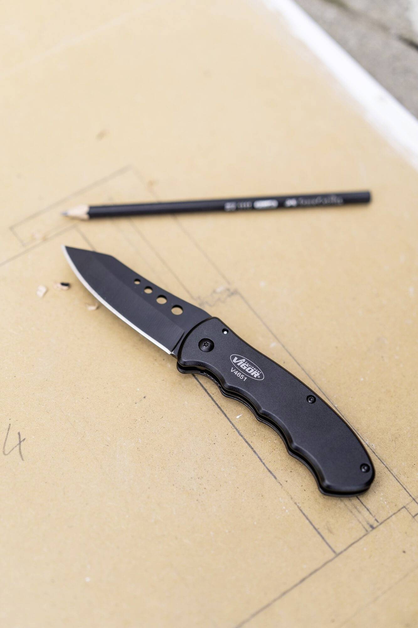 'Ein schwarzes Klappmesser und ein Bleistift liegen auf einem Blatt Papier, das mit Skizzen bedeckt ist.'