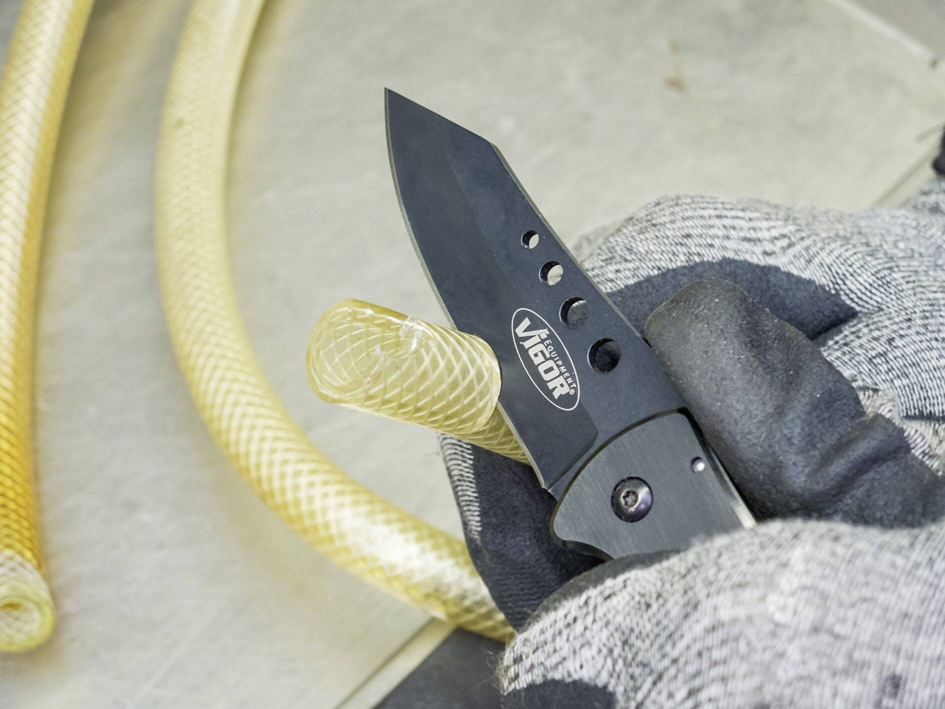 Ein behandschuhter Arbeiter hält ein schwarzes Klappmesser mit der Aufschrift 'Victor', schneidet einen gelben Schlauch.