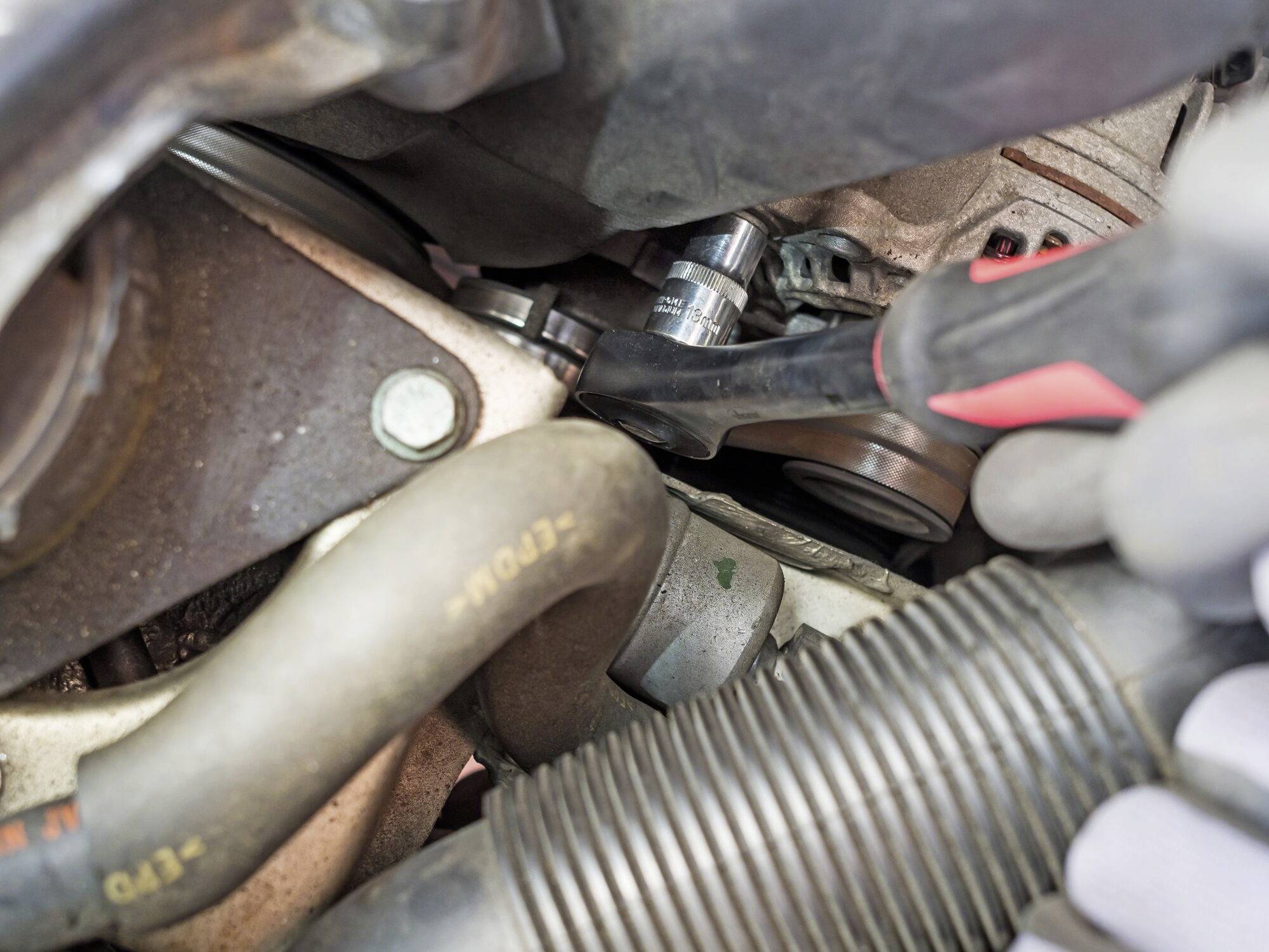 Nahaufnahme einer Autoreparatur: Ein Mechaniker verwendet einen Schraubenschlüssel, um Teile im Motorraum eines Fahrzeugs festzuziehen.