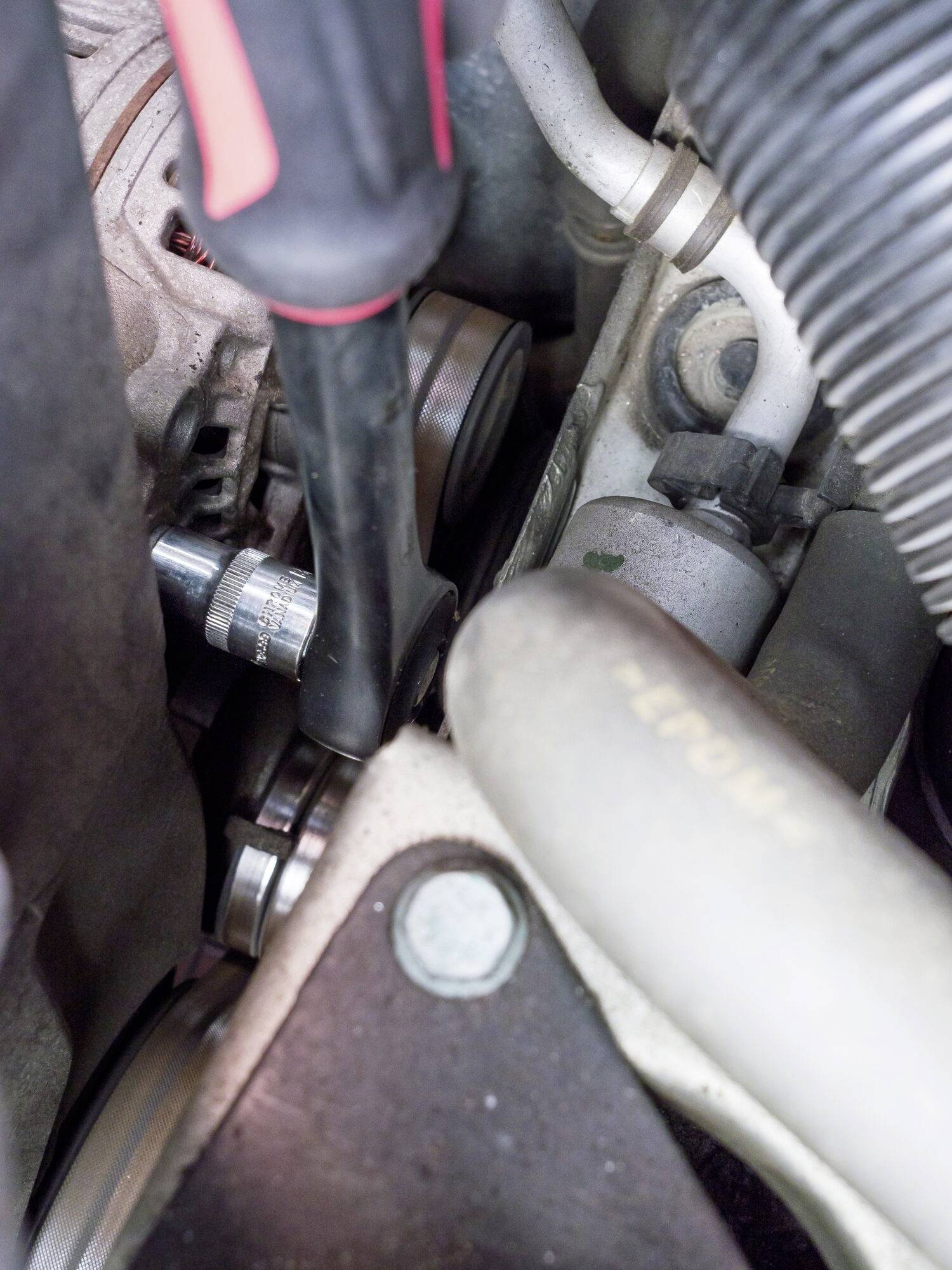 Ein Schraubenschlüssel wird genutzt, um eine Schraube im Motorraum eines Fahrzeugs zu lösen oder festzuziehen, umgeben von Schläuchen und anderen Motorkomponenten.