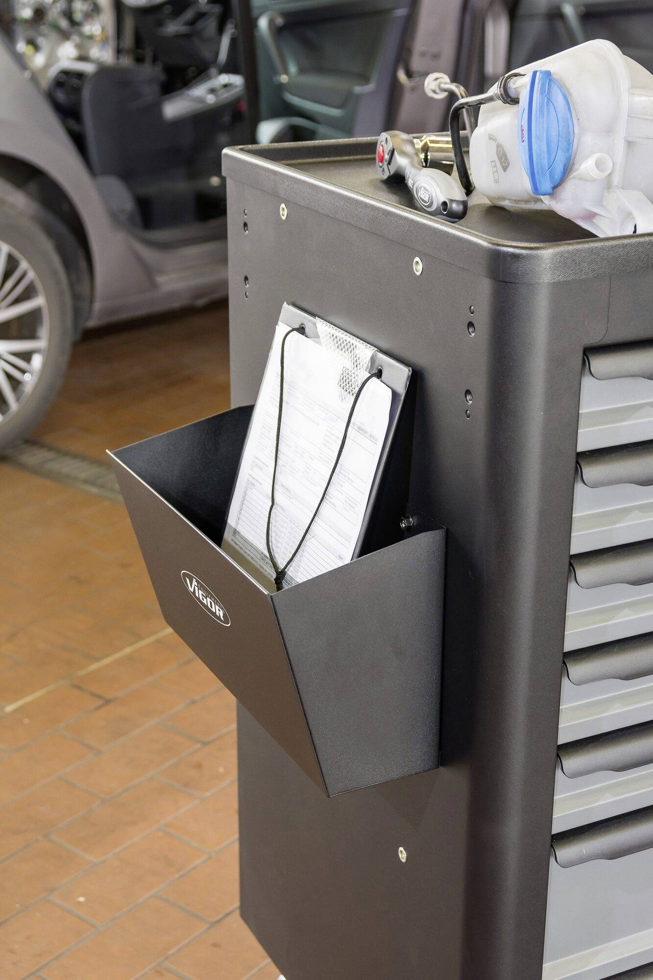 'Werkstattwagen mit Schubladen und Ablage für Dokumente, daneben ein Auto in der Werkstatt.'