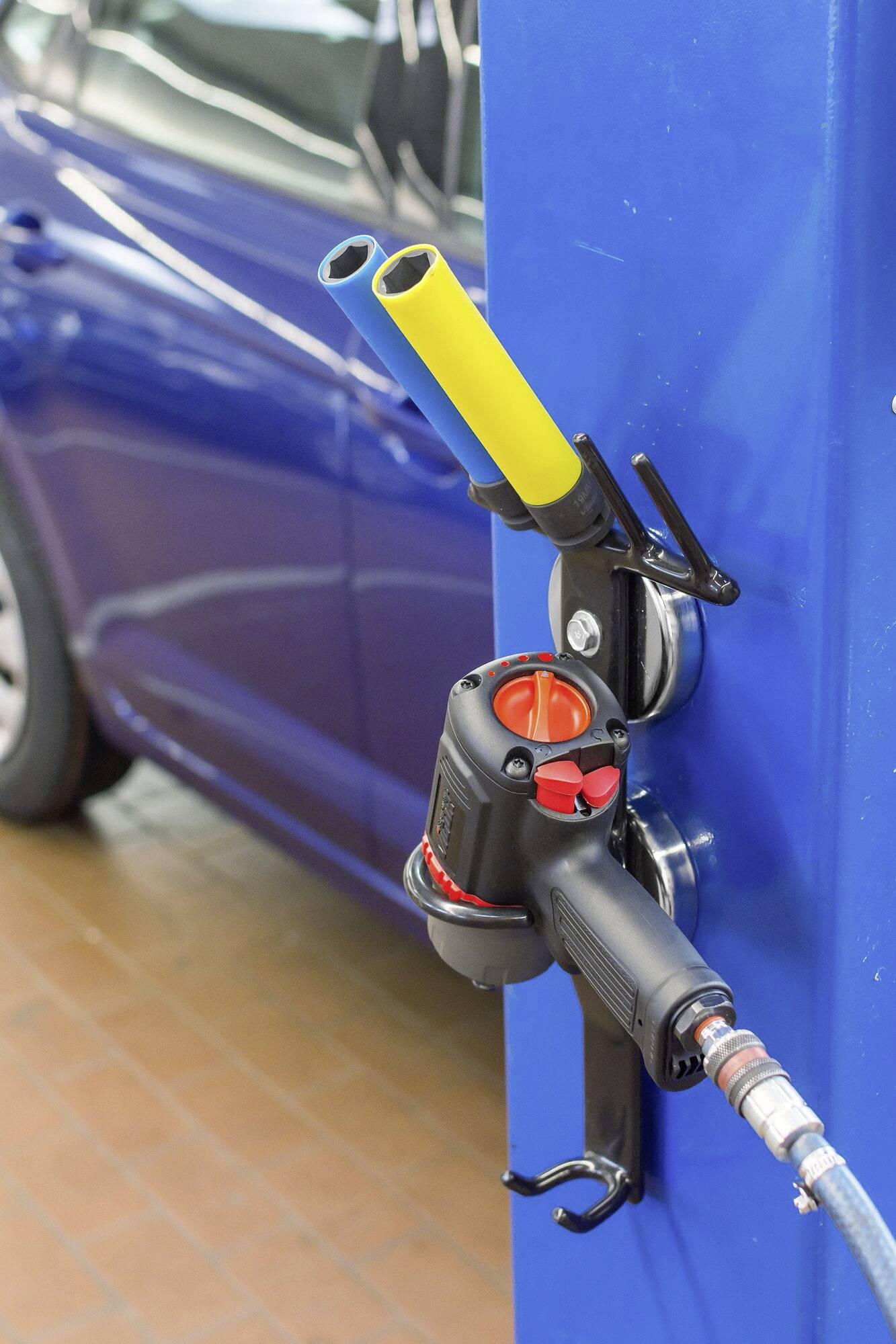 Ein blauer Pkw wird mit einem gelb-blauen Gasanschluss an einer Betankungsstation betankt. Das Auto steht auf einem Ziegelboden.
