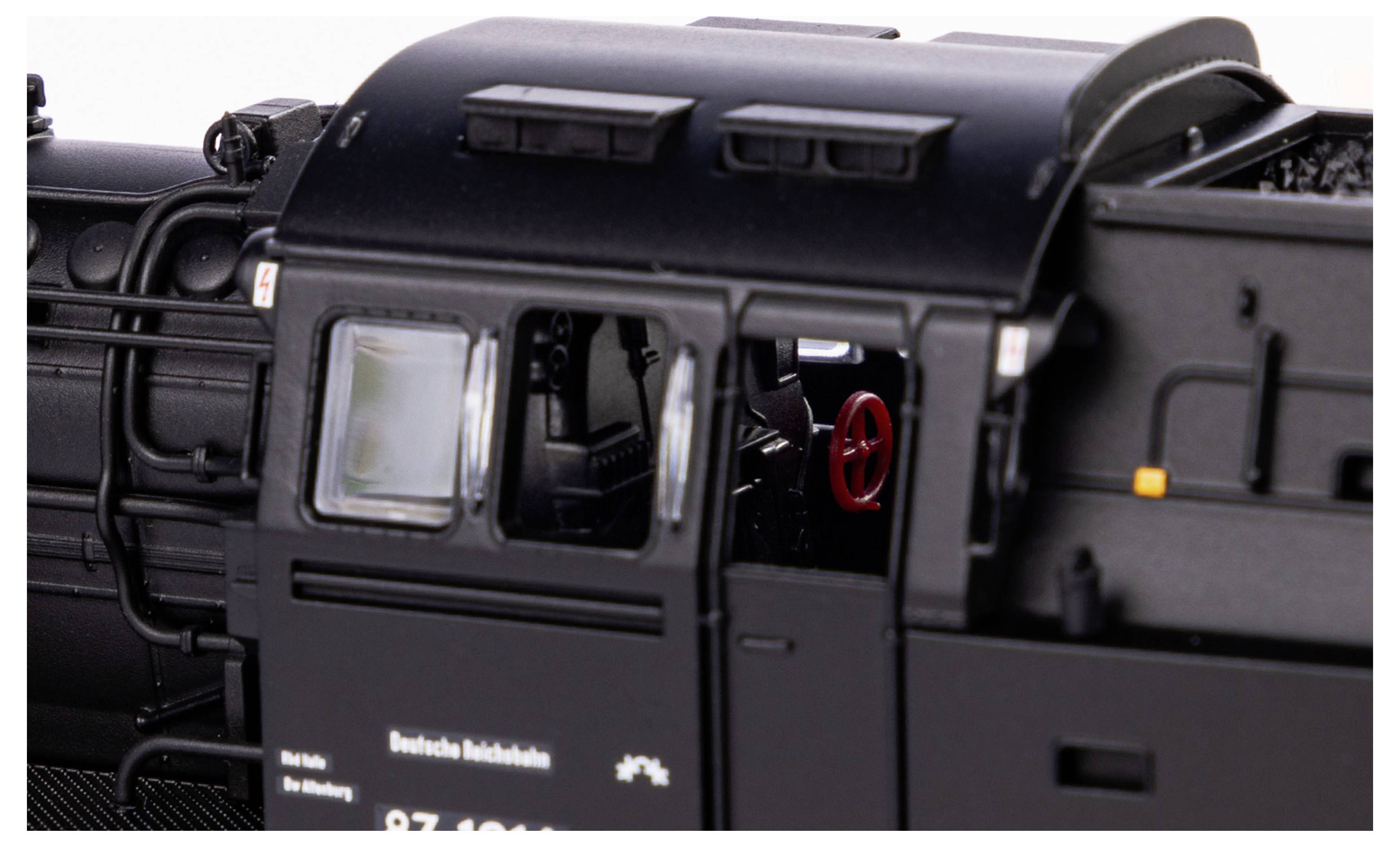 Nahaufnahme einer schwarzen Lokomotive, Fokus auf das Führerhaus mit sichtbarem roten Steuerrad und detaillierten Oberflächenstrukturen.