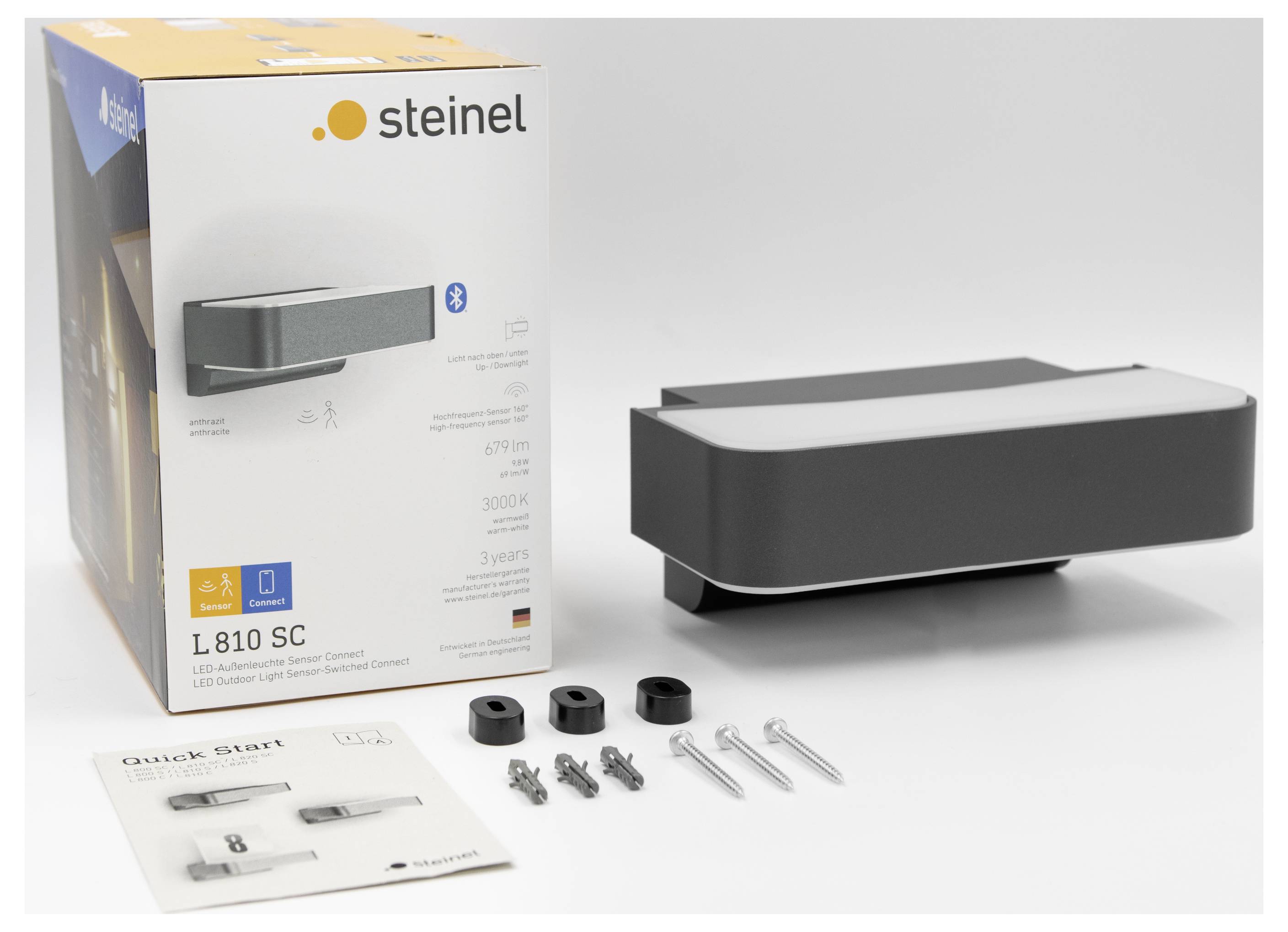 Produktfoto einer Steinel LED-Außenwandleuchte mit Verpackung, der Leuchteneinheit, Befestigungsschrauben und einer Schnellstartanleitung auf weißem Hintergrund.