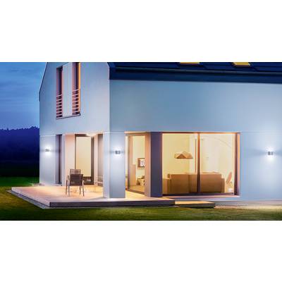 Modernes Einfamilienhaus mit großer Fensterfront, beleuchtet im Innenbereich. Terrasse mit Stühlen, umgeben von Rasen bei Abenddämmerung.