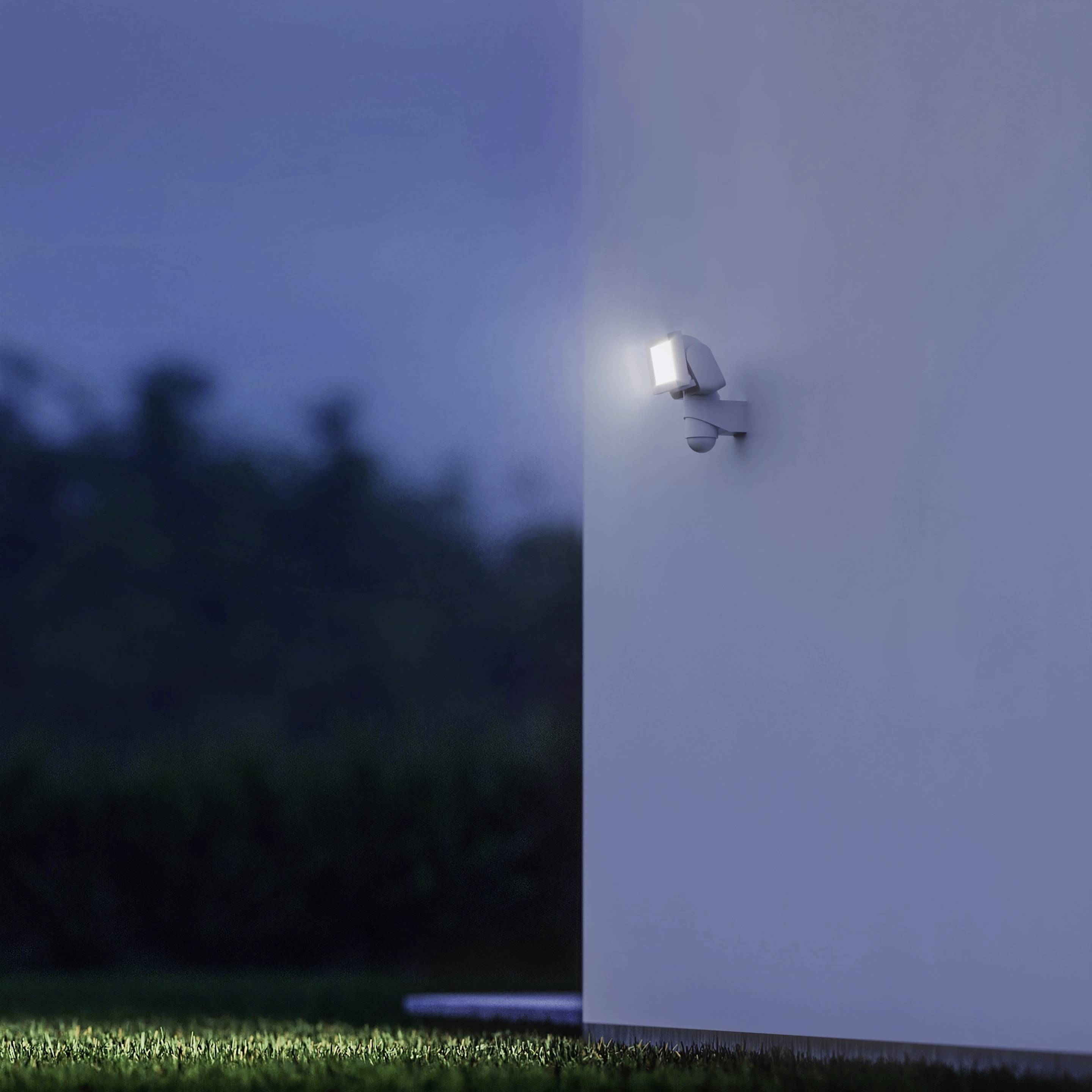 Eine helle Außenlampe beleuchtet nachts eine Hauswand. Der Hintergrund ist dunkel und unscharf, was die Lampe hervorhebt.