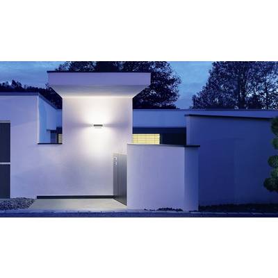 Ein modernes Haus bei Dämmerung mit eingeschaltetem Außenlicht, blauer Himmel im Hintergrund, Fenster mit hellen Lamellen sichtbar.