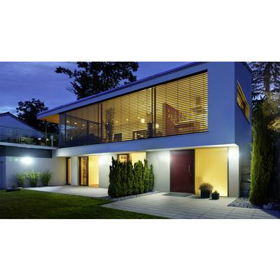 Modernes zweistöckiges Haus bei Abenddämmerung, mit großer verglaster Fassade im Obergeschoss, beleuchteter Terrasse und gepflegtem Garten.
