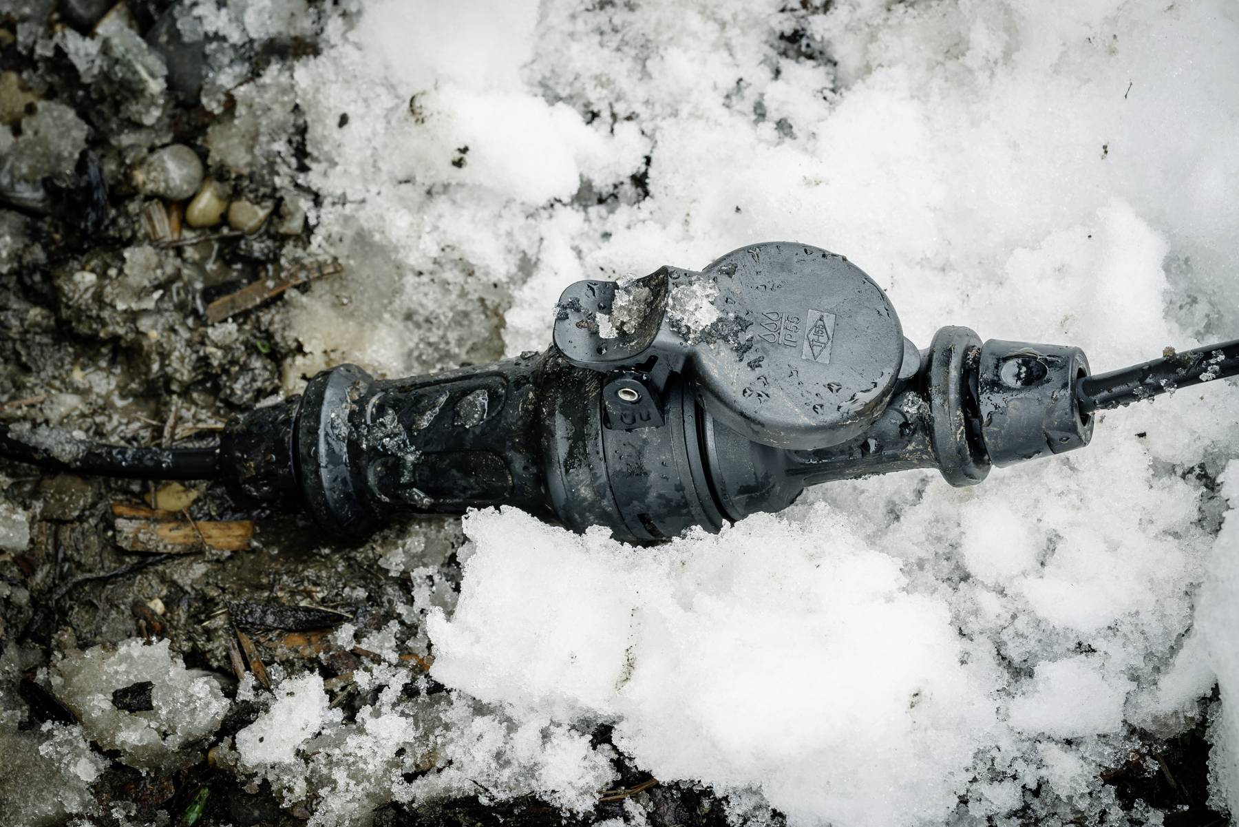 Ein schwarzer Stecker liegt im Schnee, teilweise von Matsch bedeckt, deutet auf raue Wetterbedingungen hin.