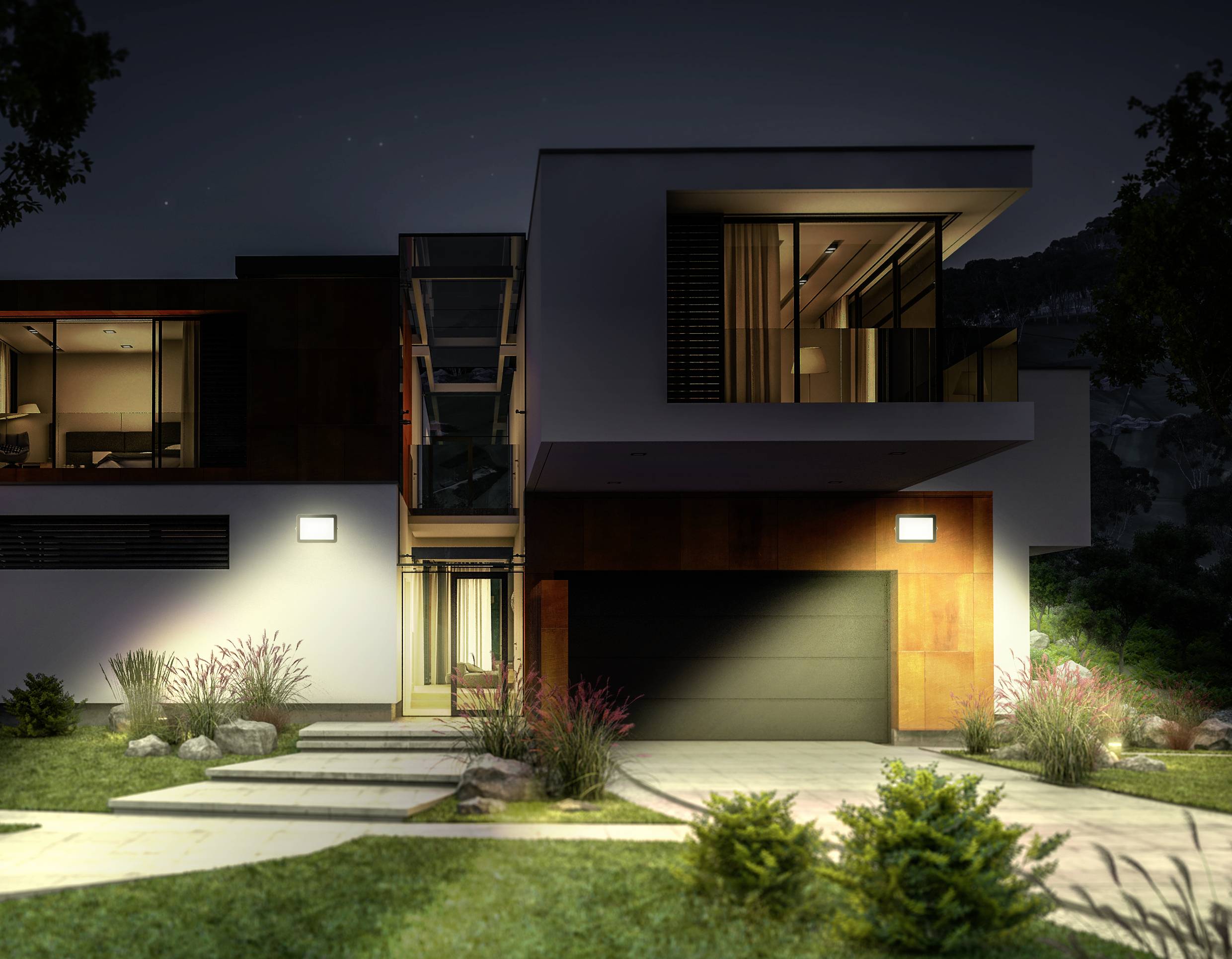 Modernes zweistöckiges Haus bei Nacht, beleuchtet. Große Fenster, gepflasterter Gehweg, gepflegter Garten im Vordergrund.