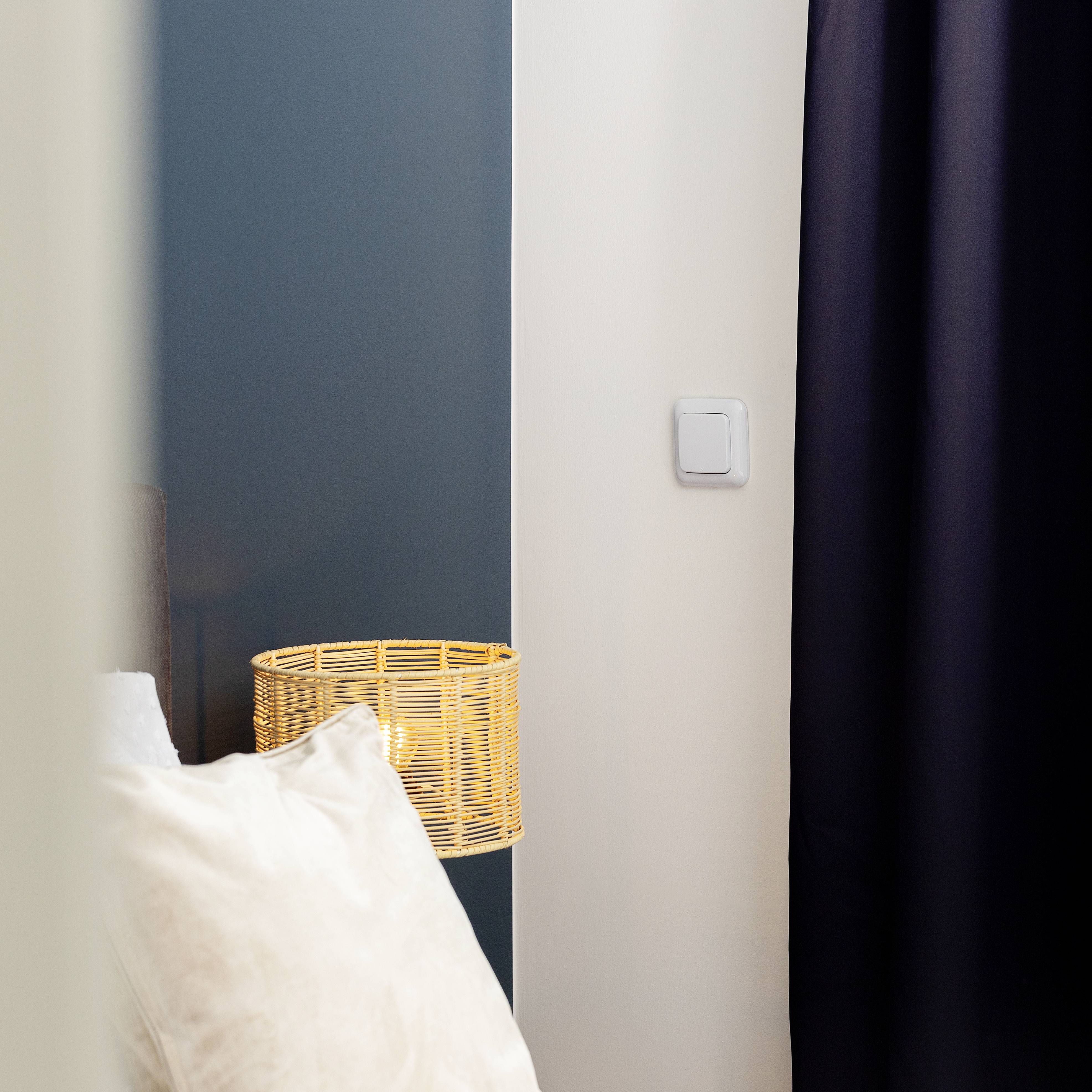 Ein gemütliches Zimmer mit einem weißen Kissen im Vordergrund und einem runden, geflochtenen Lampenschirm auf einem Tisch.