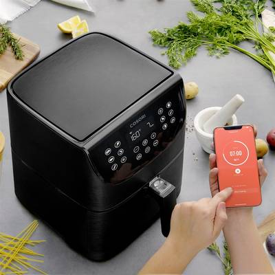 Eine Person stellt einen Timer auf einem Smartphone ein, während sie neben einer Heißluftfritteuse steht, um zu kochen.