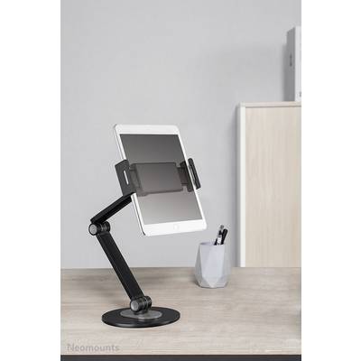 'Ein Tablet steht in einem verstellbaren schwarzen Halter mit Arm auf einem Schreibtisch. Im Hintergrund sind ein Stifthalter und ein Schrank.'